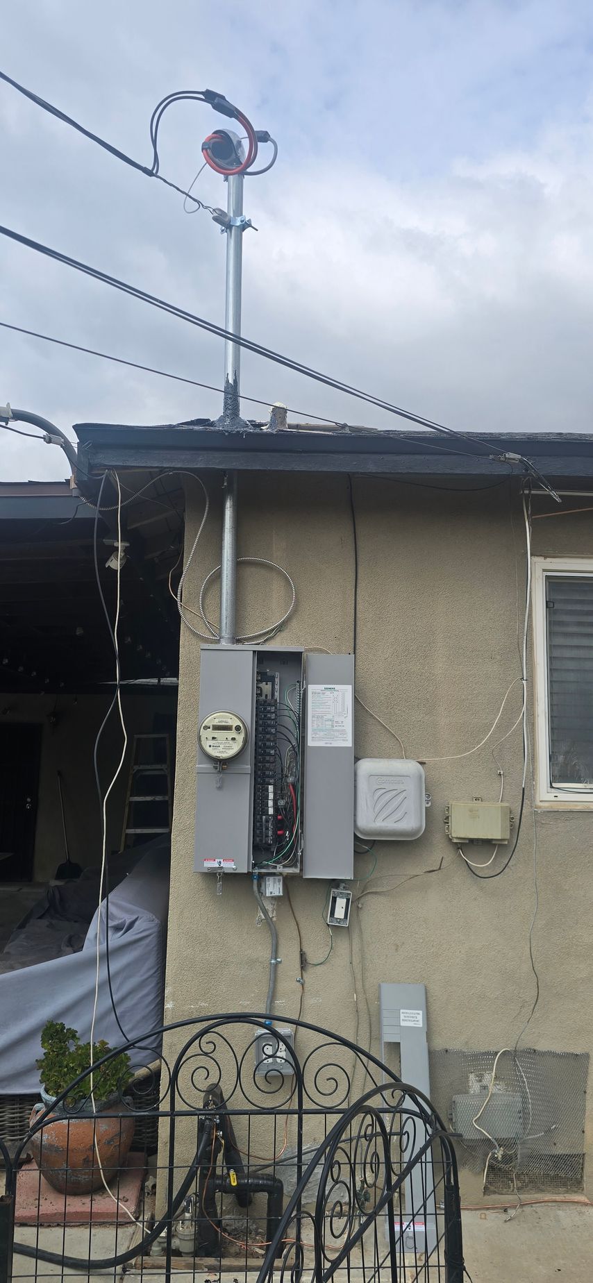 Exterior of a beige house with utility meters, cables, and a small wind turbine on the roof