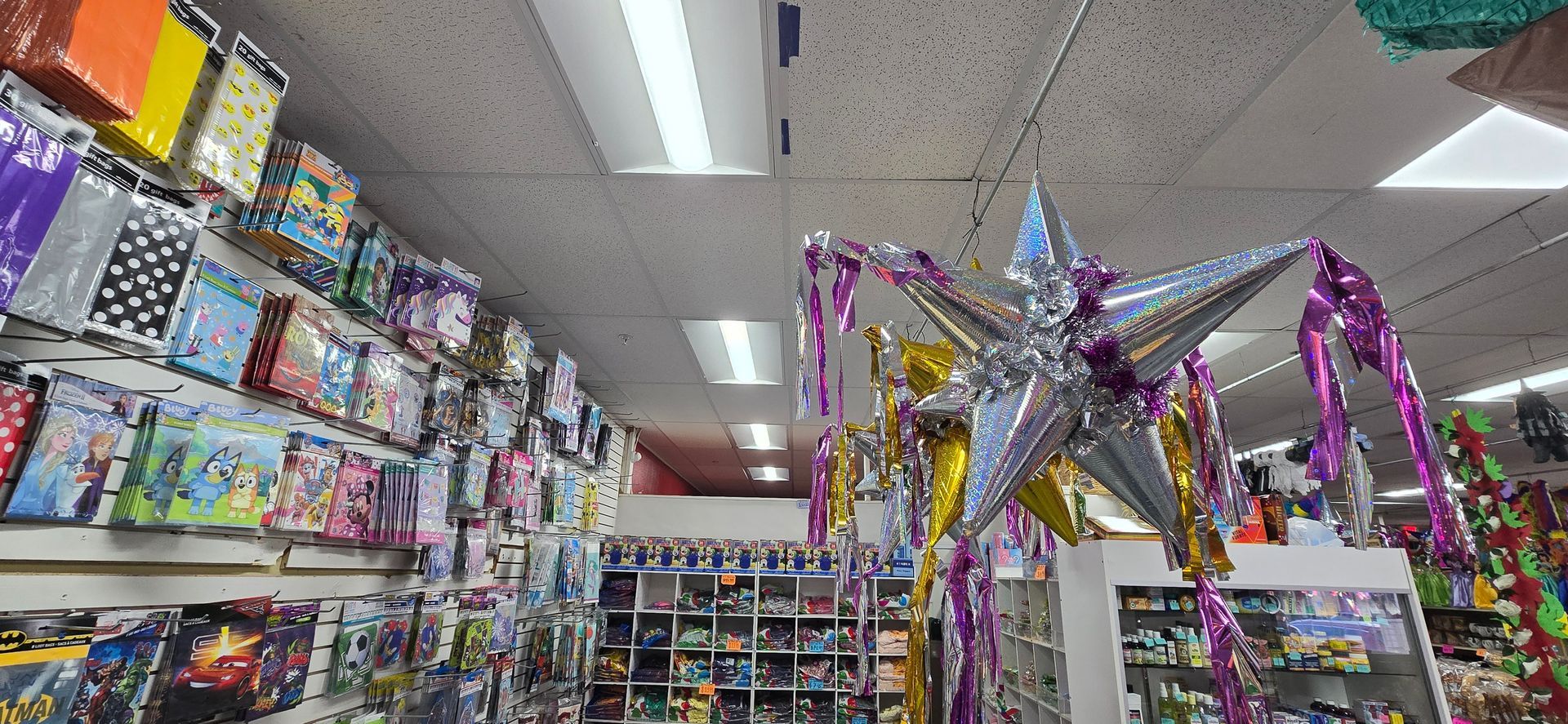 A party supply store aisle with colorful decorations, balloons, and streamers hanging from the ceiling.