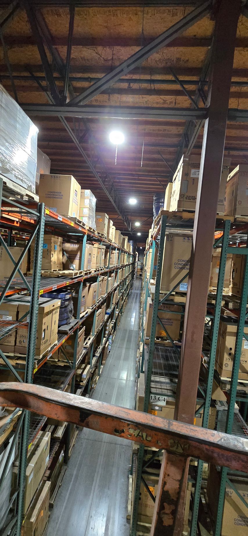 Warehouse aisle with tall metal shelving, stacked boxes, and bright overhead lights