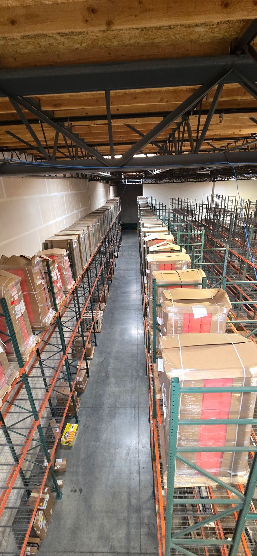 Warehouse aisle with tall metal racks stacked with boxes and supplies under exposed ceiling beams