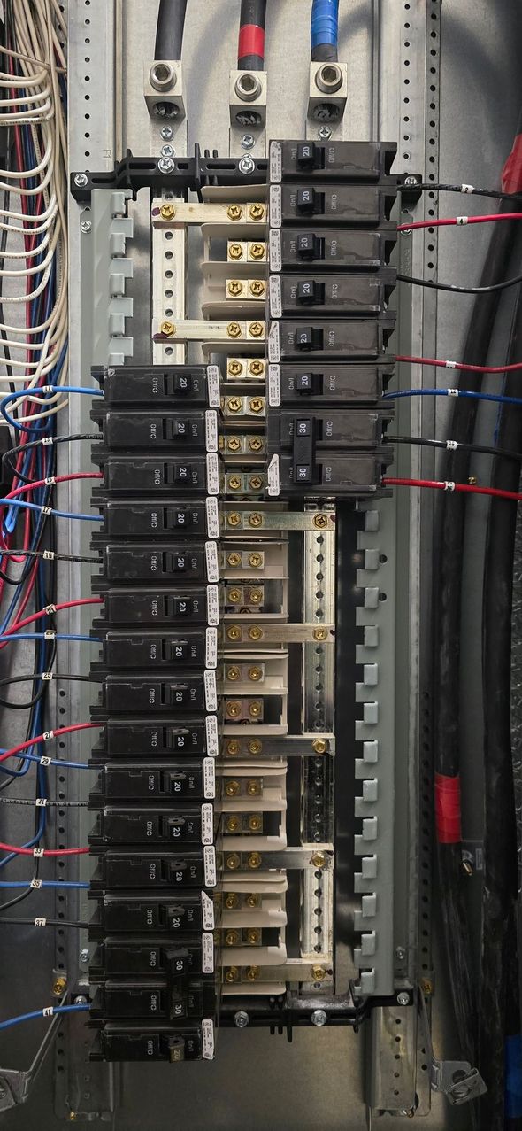 Electrical breaker panel with rows of circuit breakers and red and black wiring.