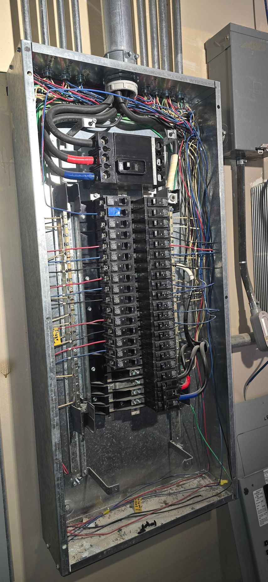Open electrical panel with exposed wiring, breakers, and cable bundles inside a metal cabinet