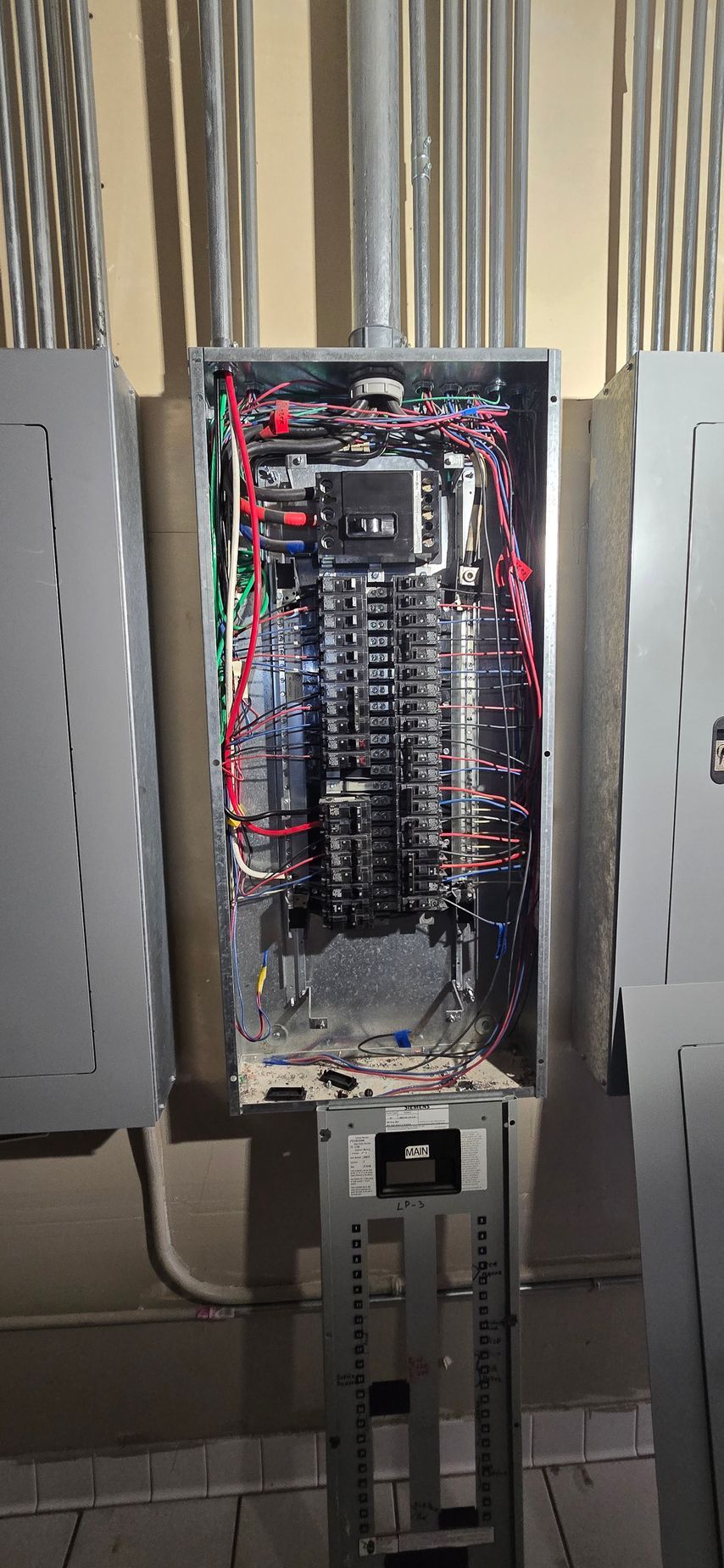 Open electrical breaker panel with exposed wiring and rows of circuit breakers in a utility room