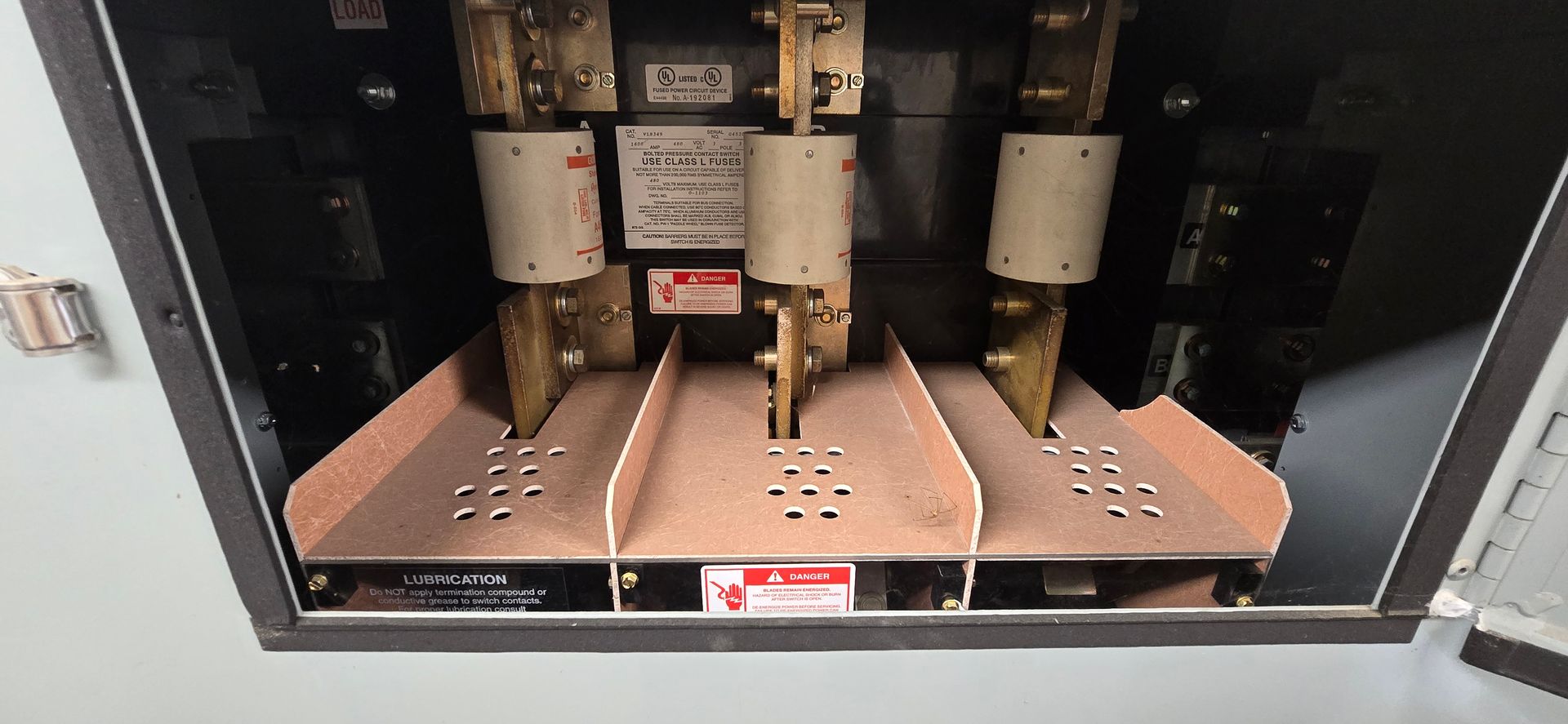 Open electrical cabinet with copper bus bars, switches, and wiring inside.