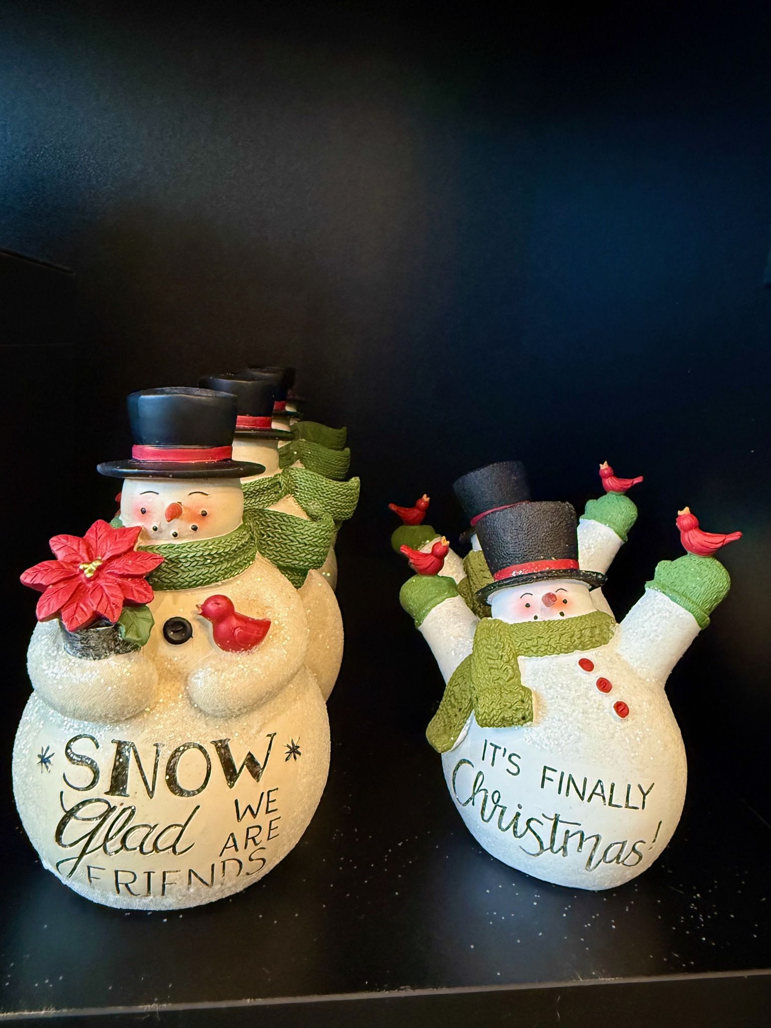 Two snowmen are sitting on a black shelf.
