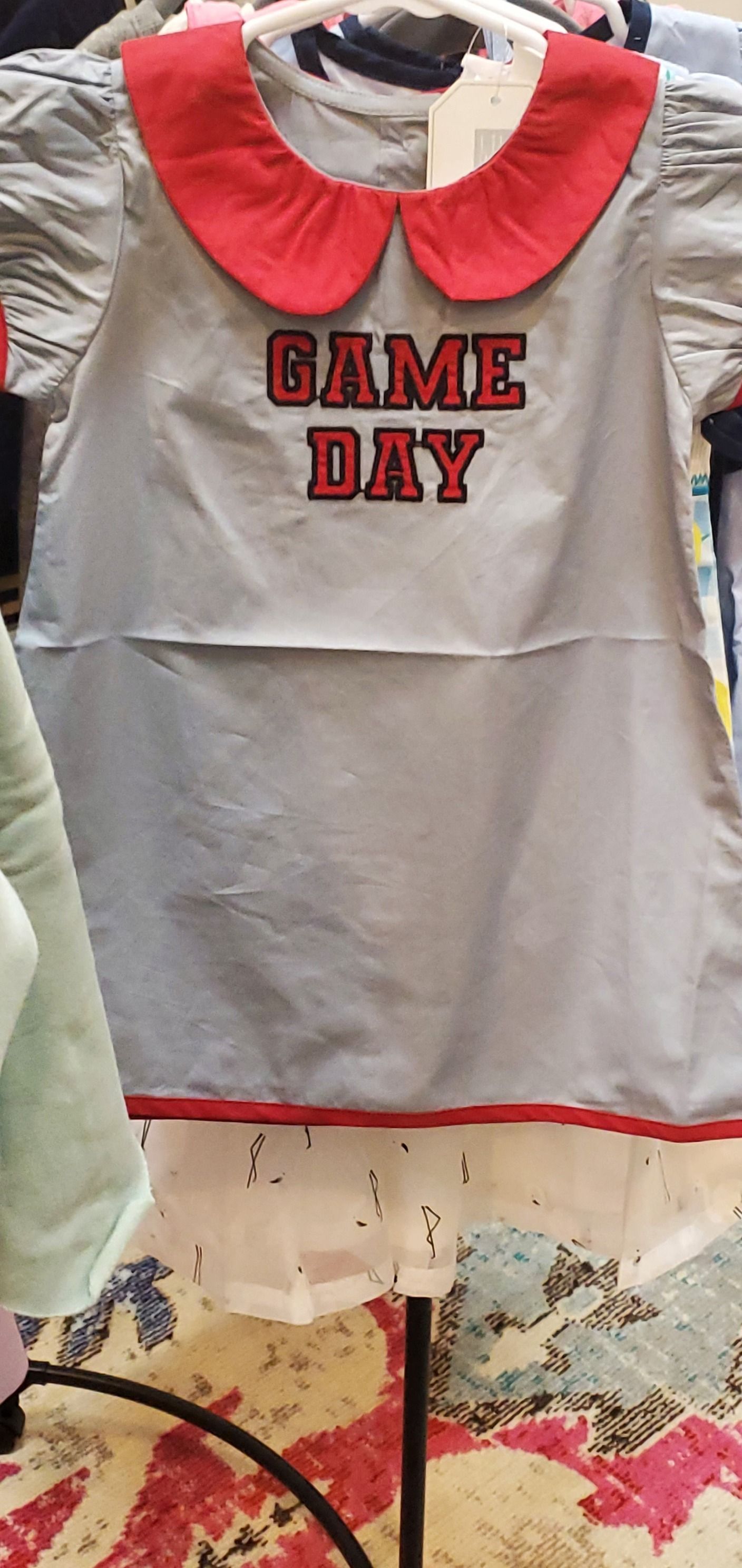 A dress with a red collar and the words `` game day '' on it is hanging on a hanger.