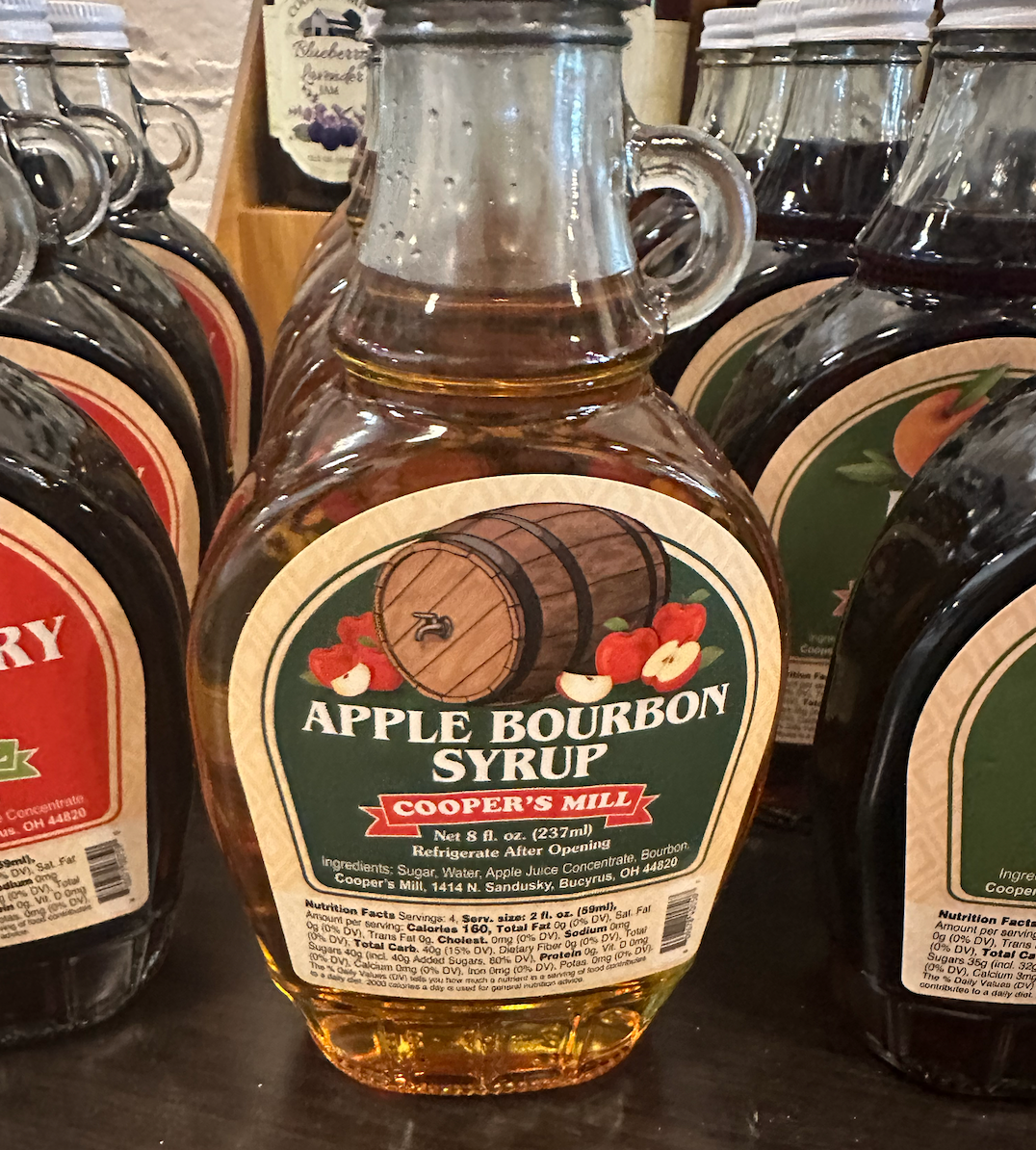 A bottle of apple bourbon syrup with a wooden barrel and apple on the label