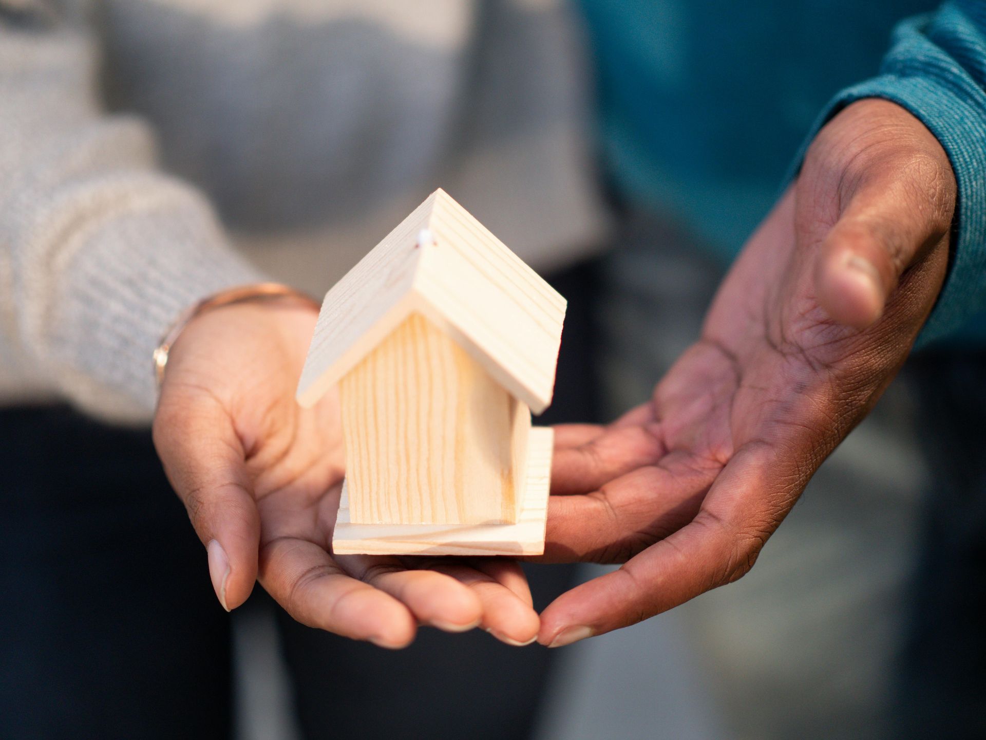 A man and a woman are holding a small wooden house in their hands.