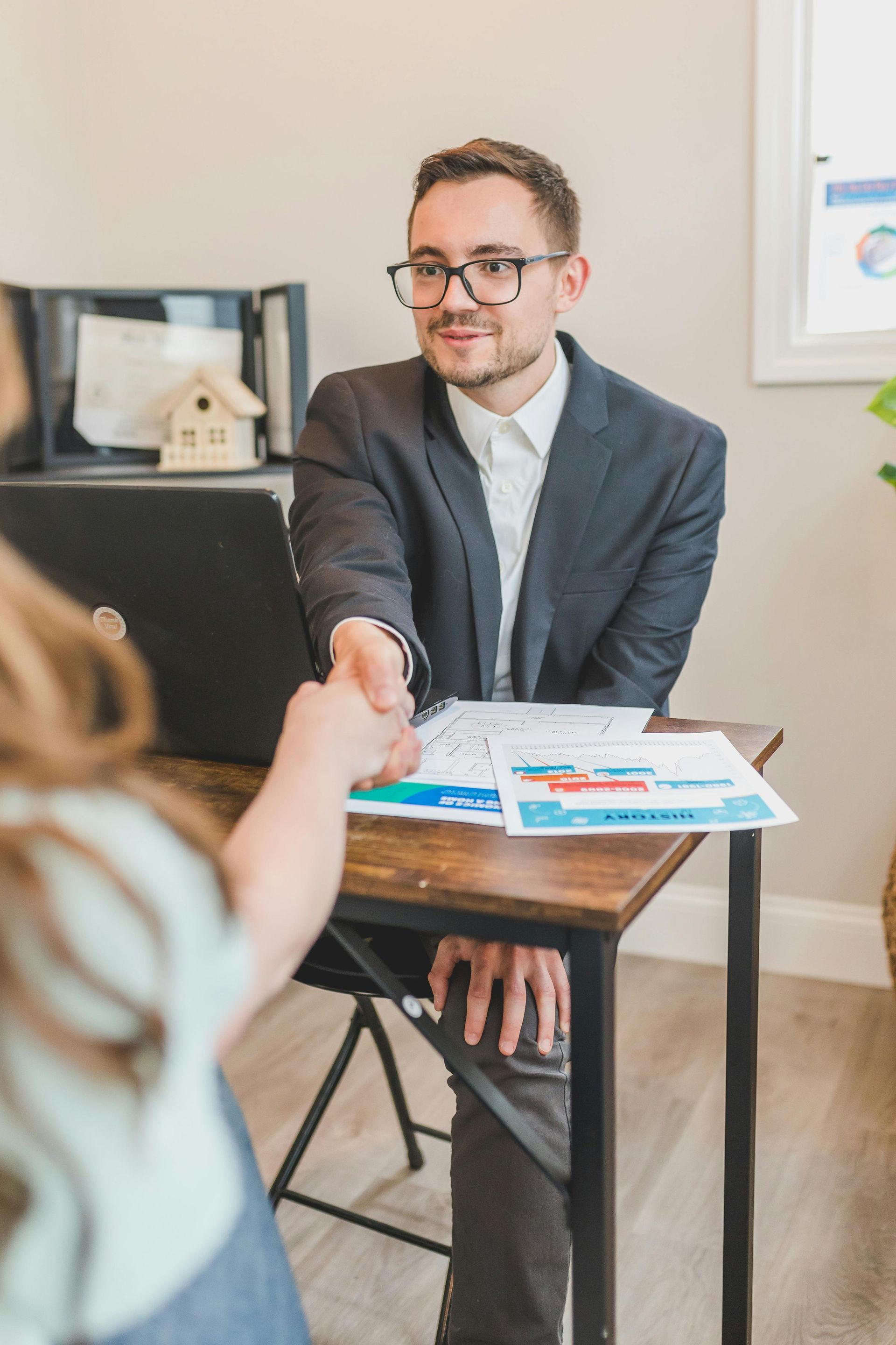 A man in a suit is shaking a woman 's hand while sitting at a desk.