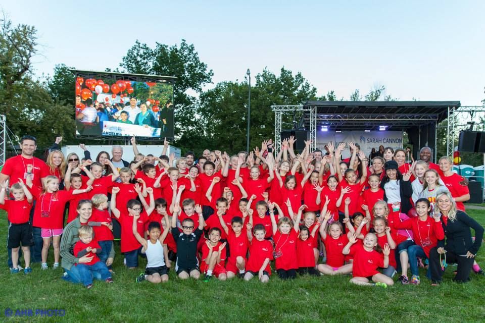 A large group of children are posing for a picture in front of a large screen.