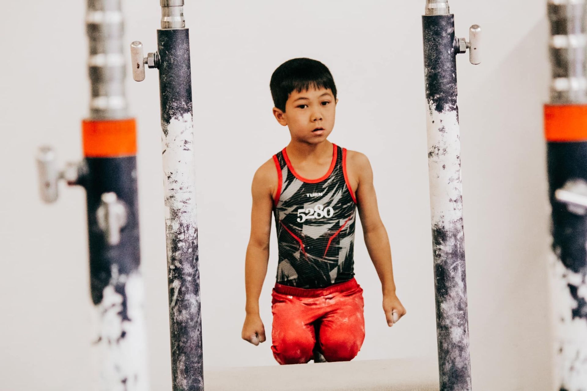 A young boy is doing exercises on parallel bars in a gym.