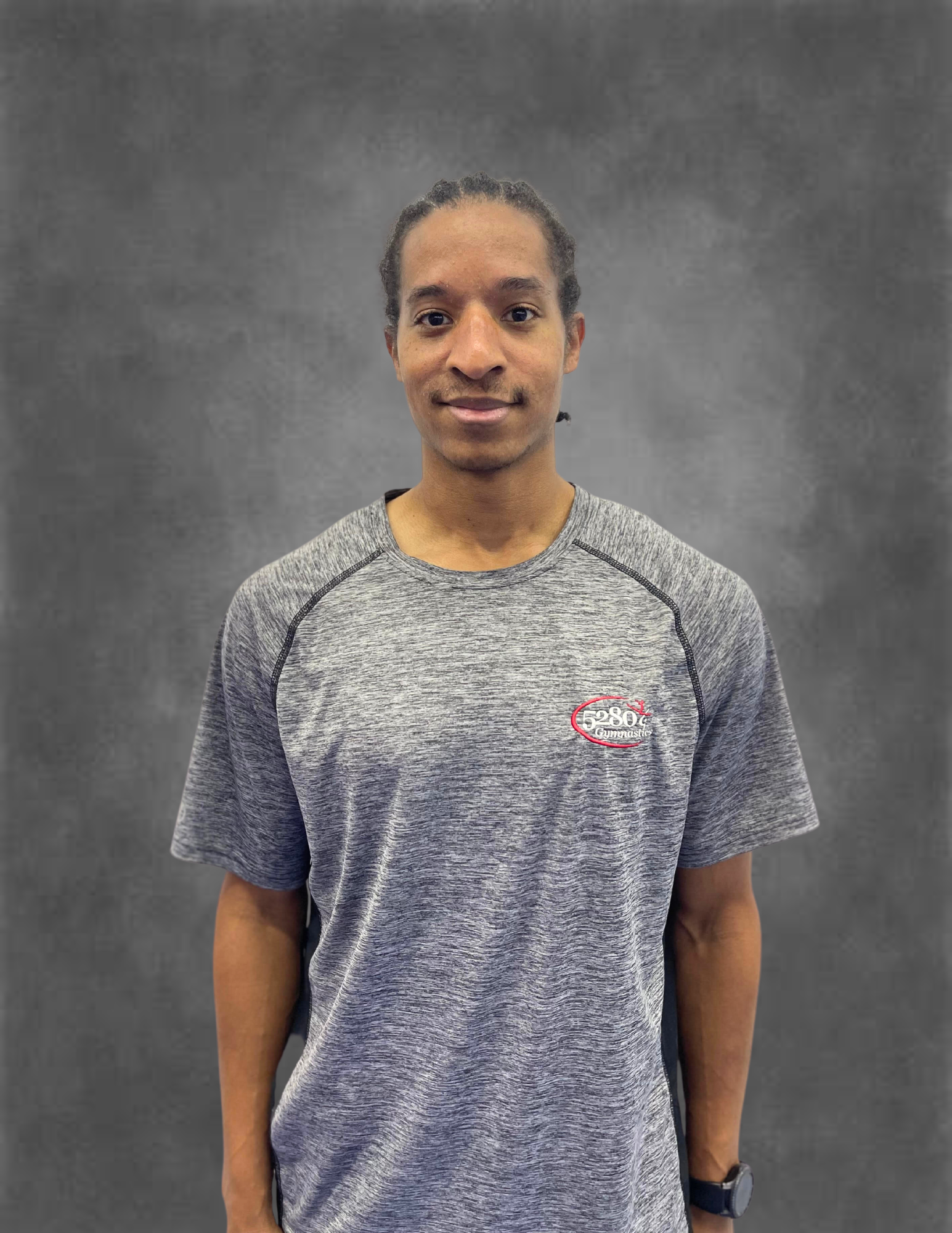 A man wearing a grey t-shirt is standing in front of a gray background.