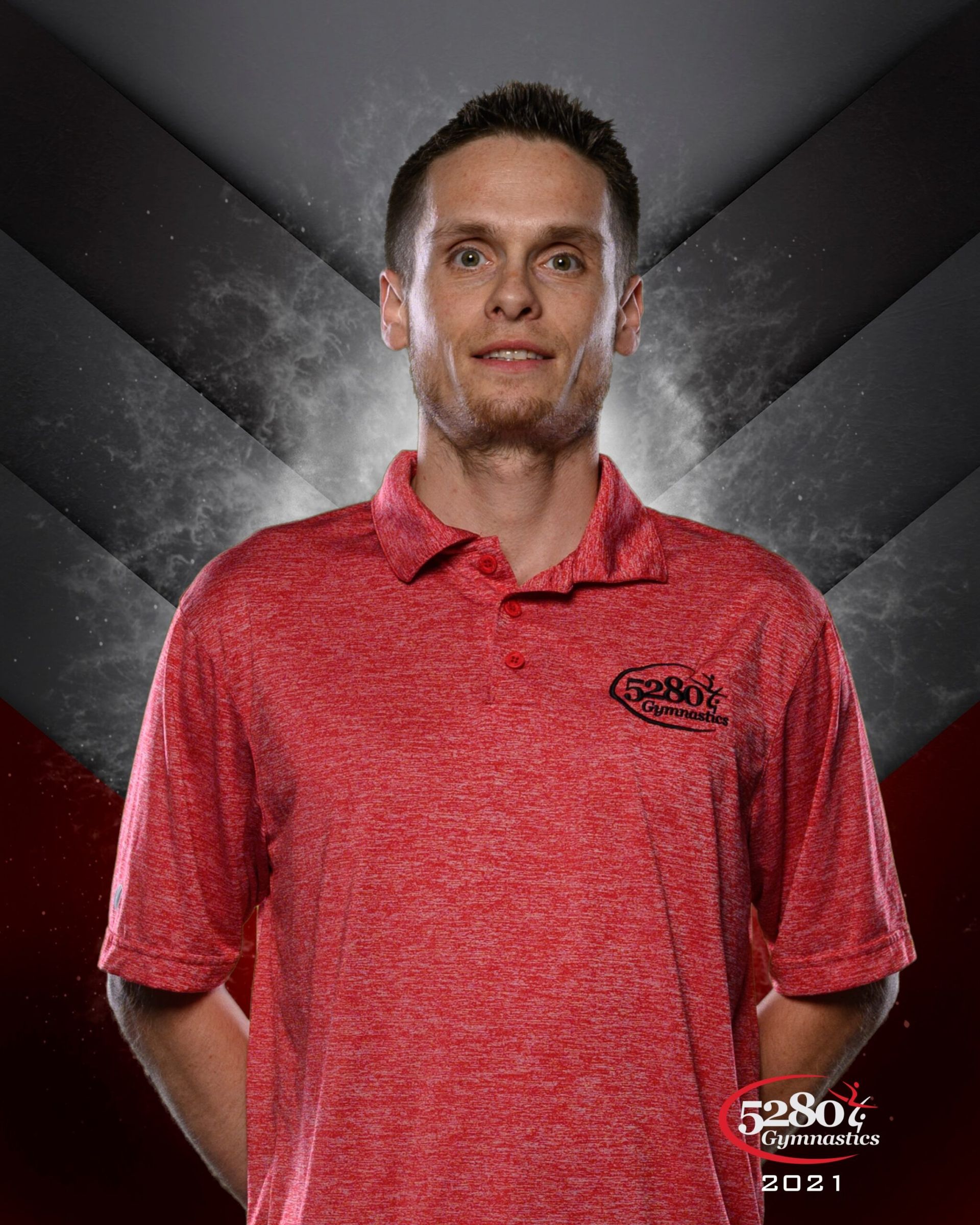 A man in a red shirt is standing in front of a dark background.