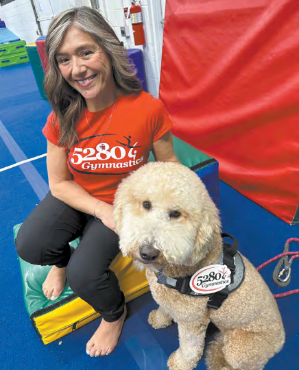 A woman wearing a 5280 gymnastics shirt sits next to a small dog