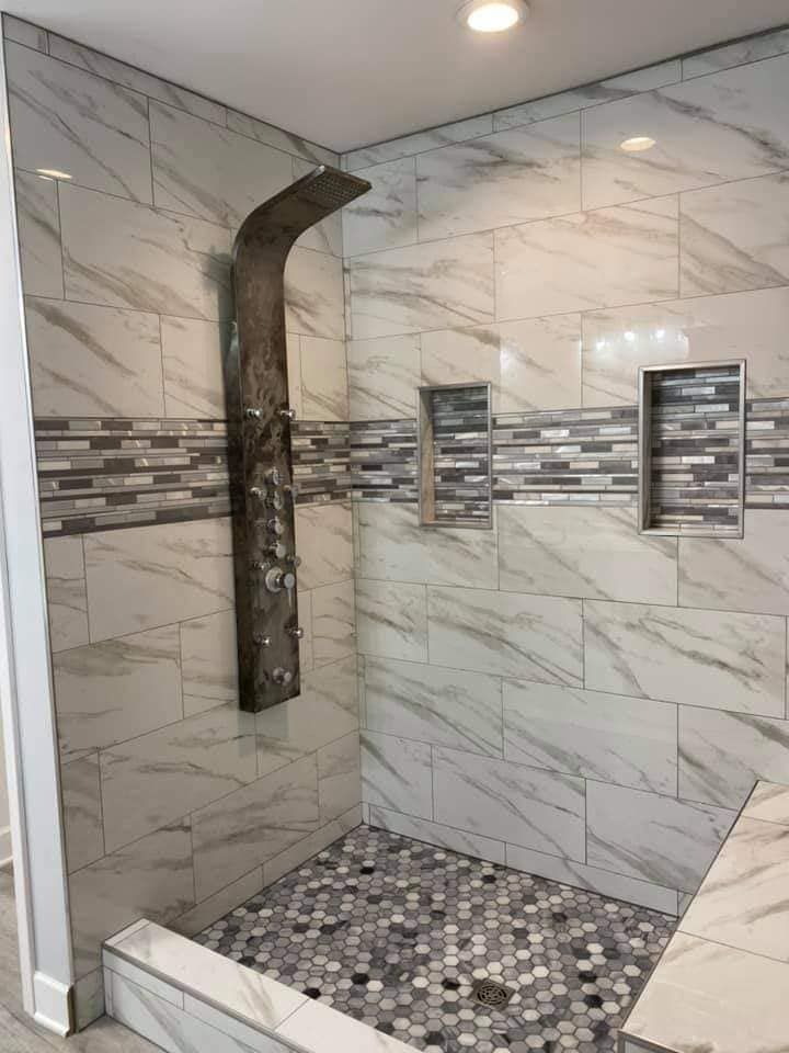 Modern shower with marble-look tiles, mosaic floor, built-in shelves, and a unique, rustic showerhead.