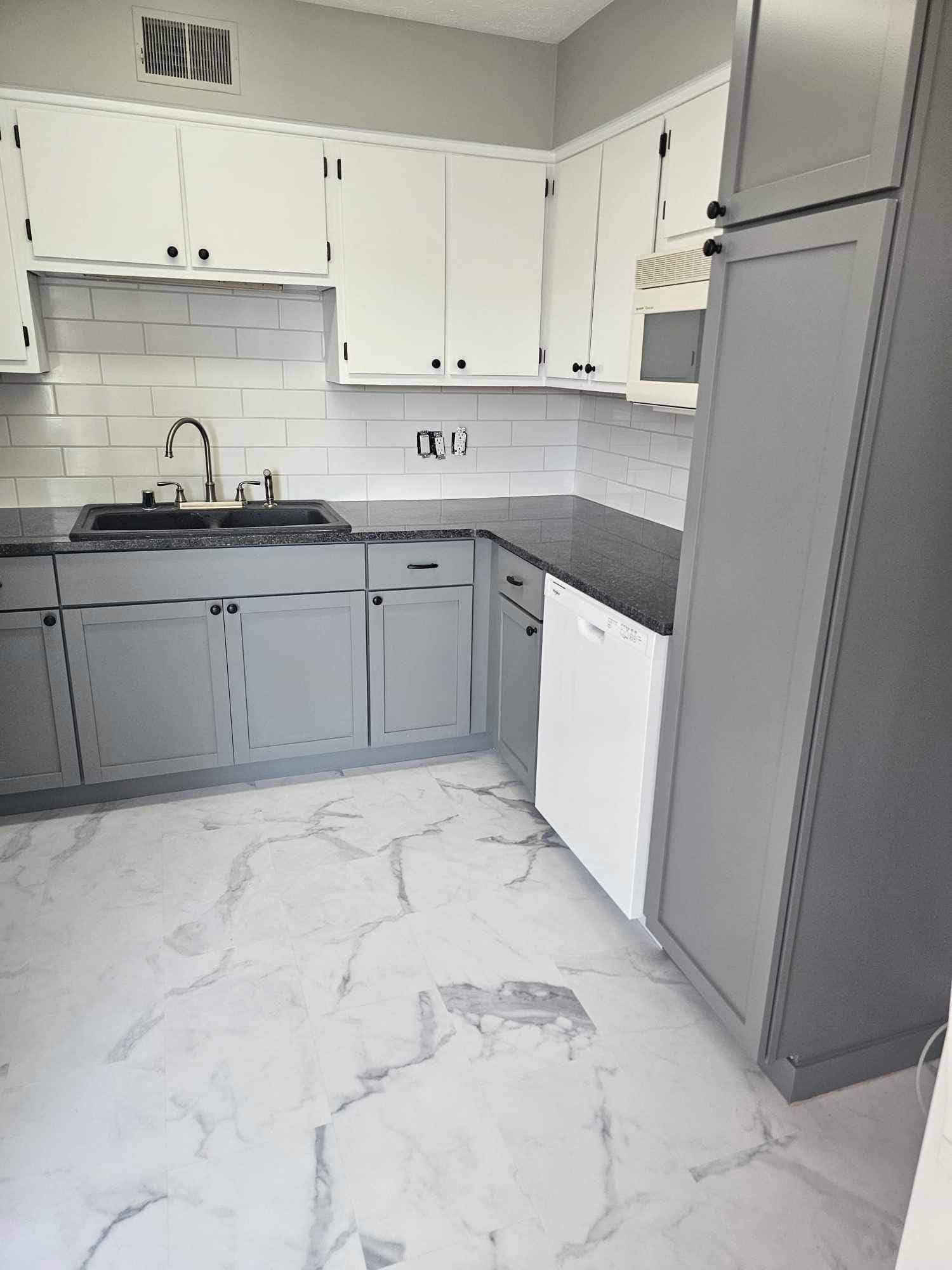 Kitchen with white and grey cabinets, subway tile backsplash, and marble-look flooring.