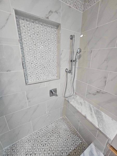 Tiled shower with marble-look walls, pebbled floor, built-in bench and niche. Silver shower fixtures.