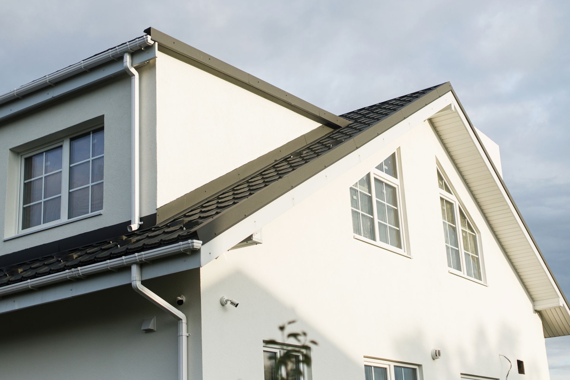 White two-story house with dark roof, windows, and gutters against a cloudy sky.