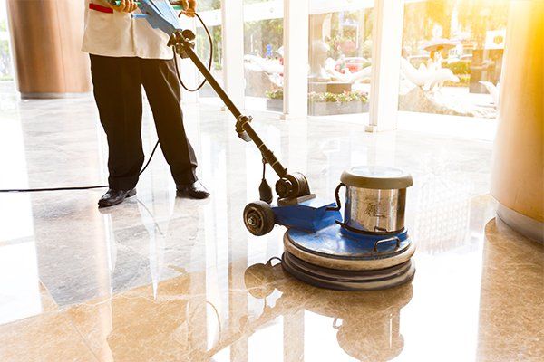 A person polishing a waxed floor to a high shine, using a floor polisher machine.