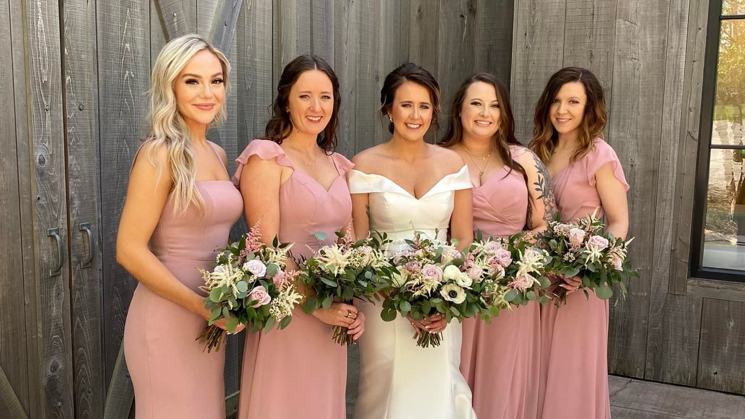 a bride and her bridesmaids are posing for a picture in front of a wooden building .