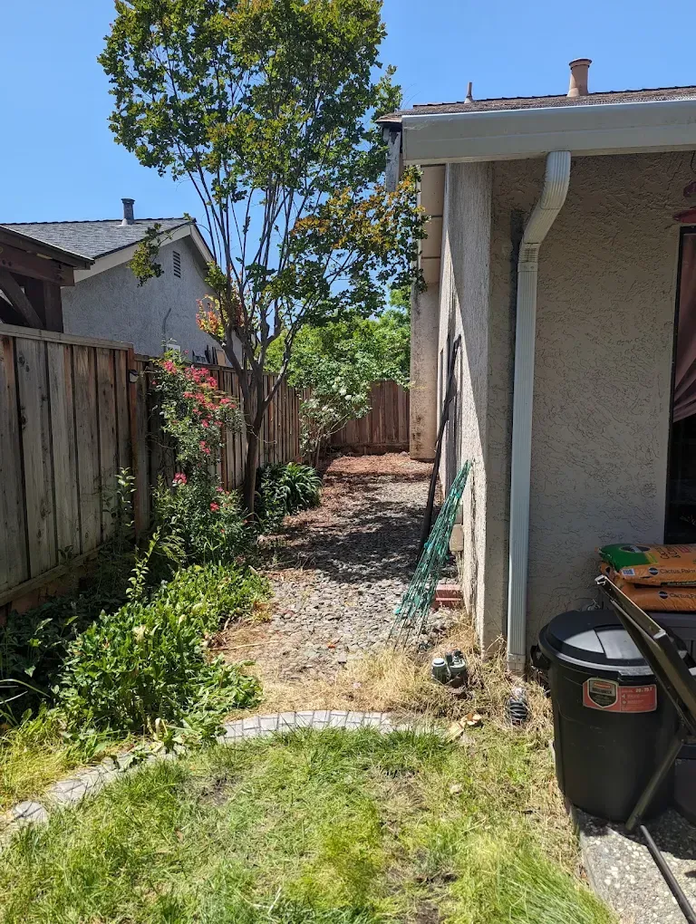 A backyard with a fence and a trash can in front of a house.