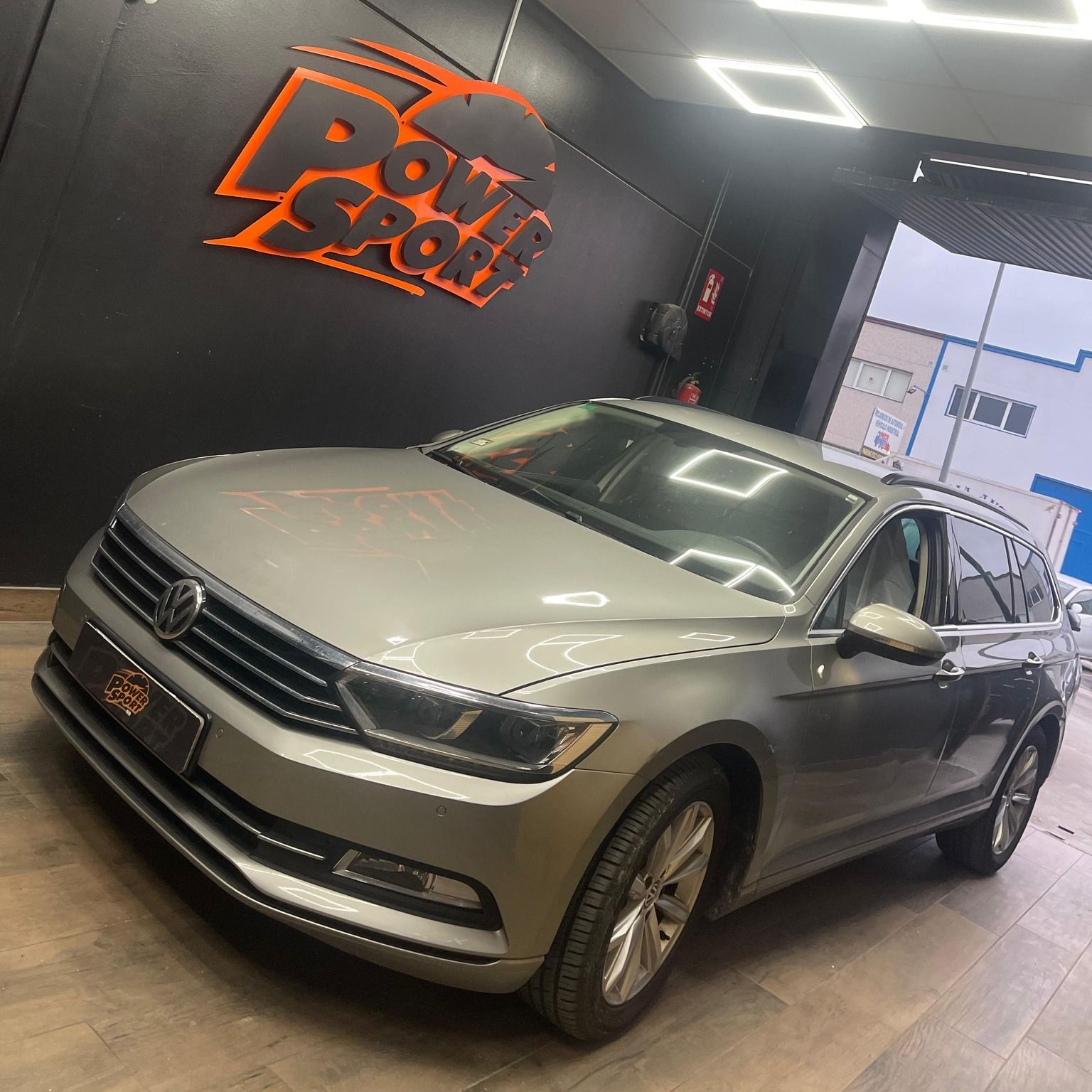 Un Volkswagen familiar plateado estacionado en el interior, frente a una pared negra con el logotipo naranja 