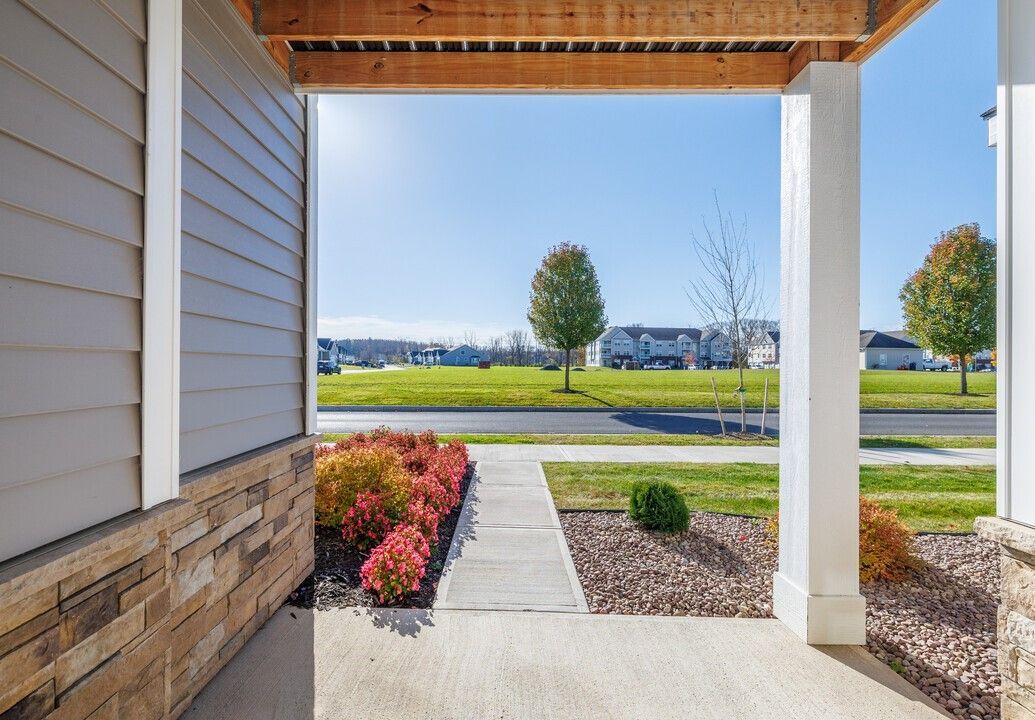 A porch with a view of a grassy field and a house in the background.