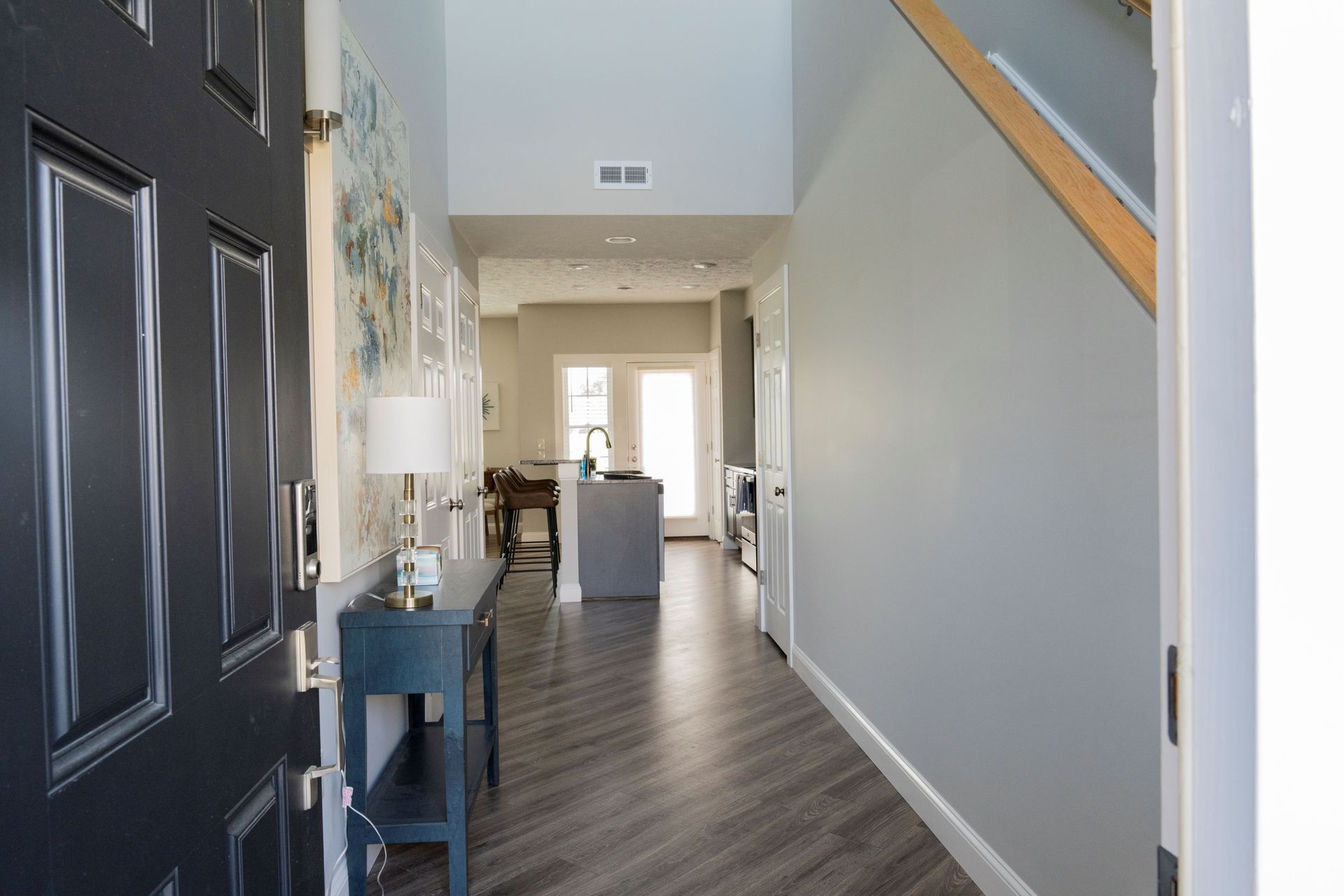 A hallway with a black door leading to a living room and stairs.