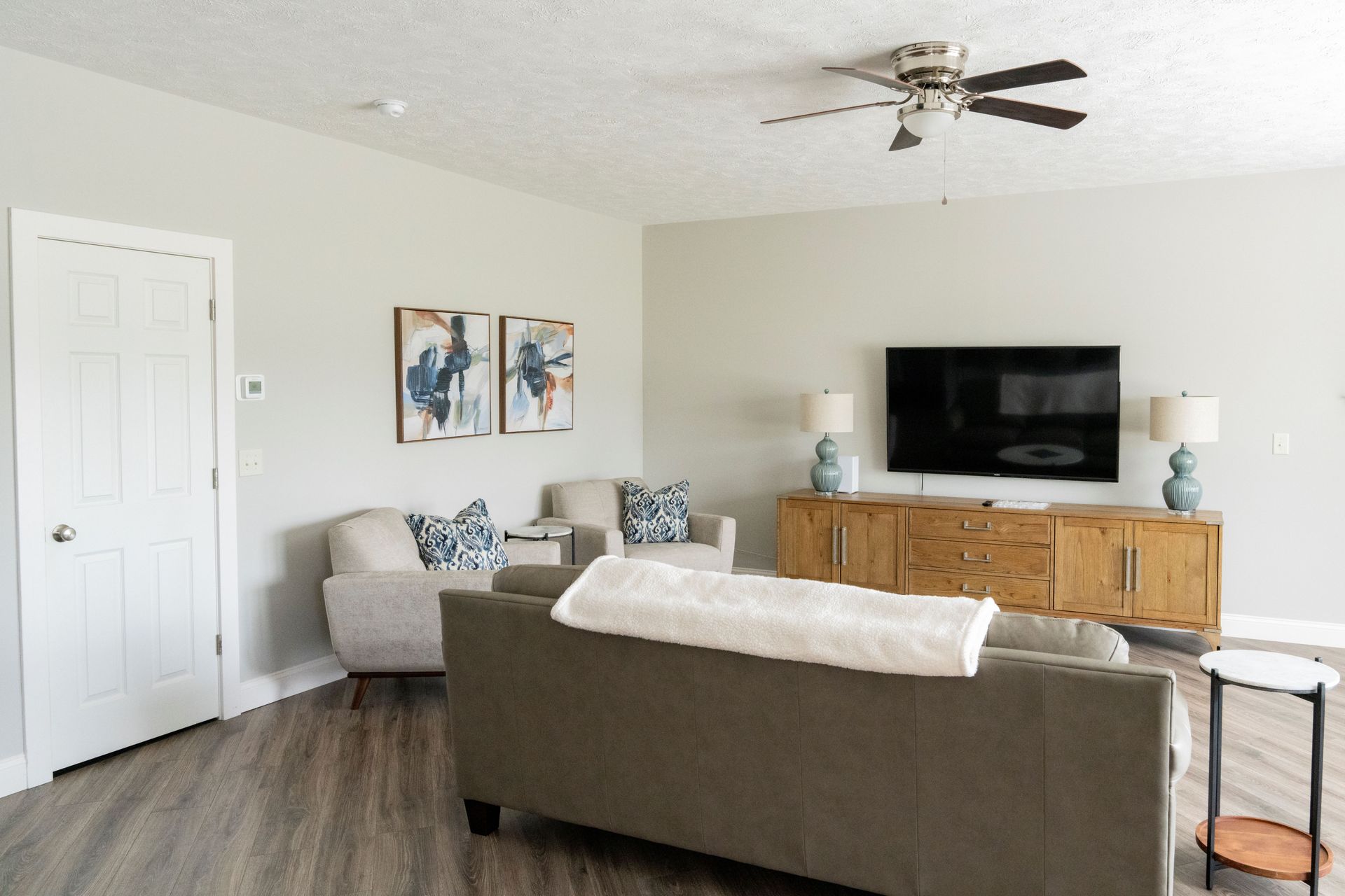 A living room with a couch , chairs , a television and a ceiling fan.
