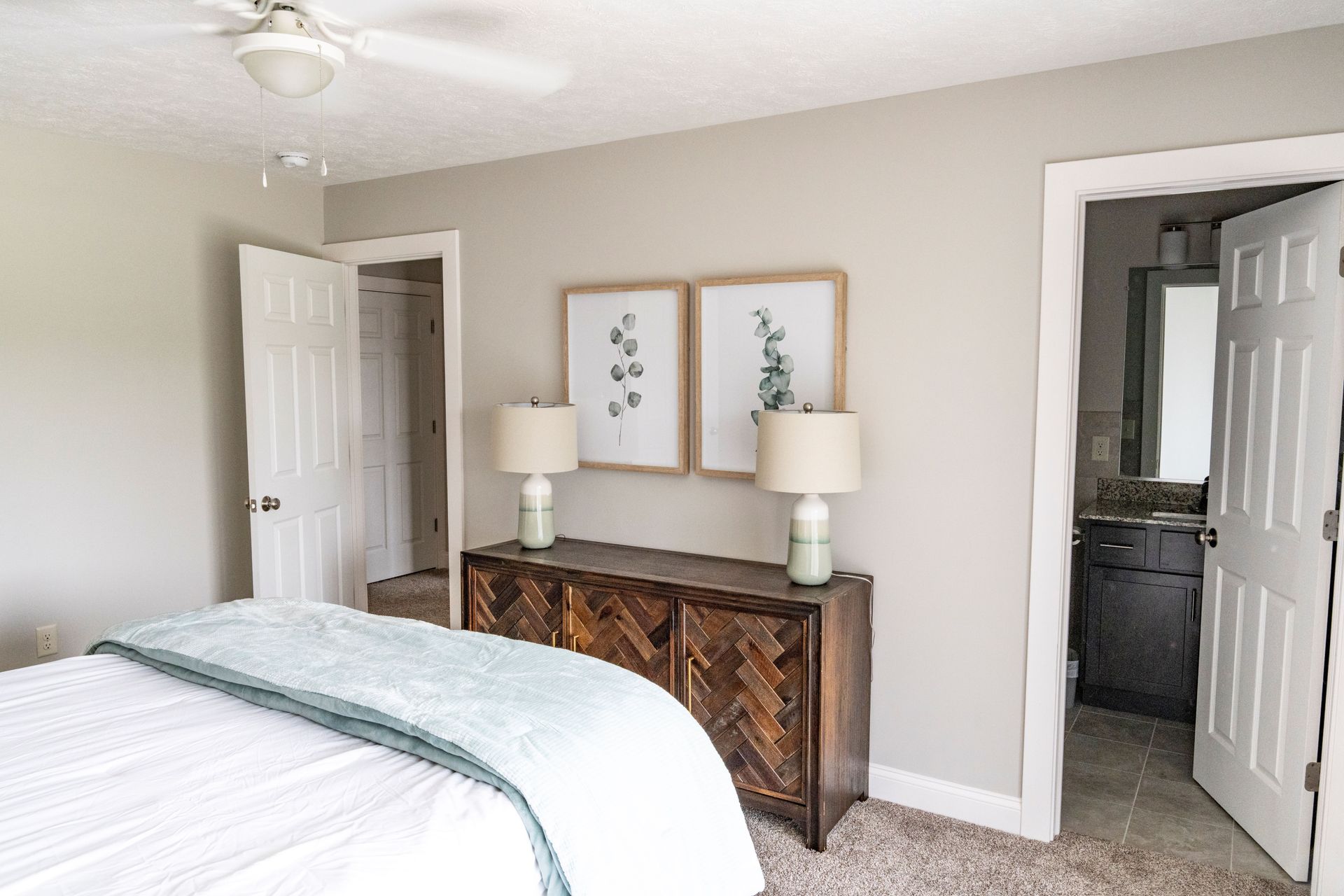 A bedroom with a bed , dresser , lamps and a ceiling fan.