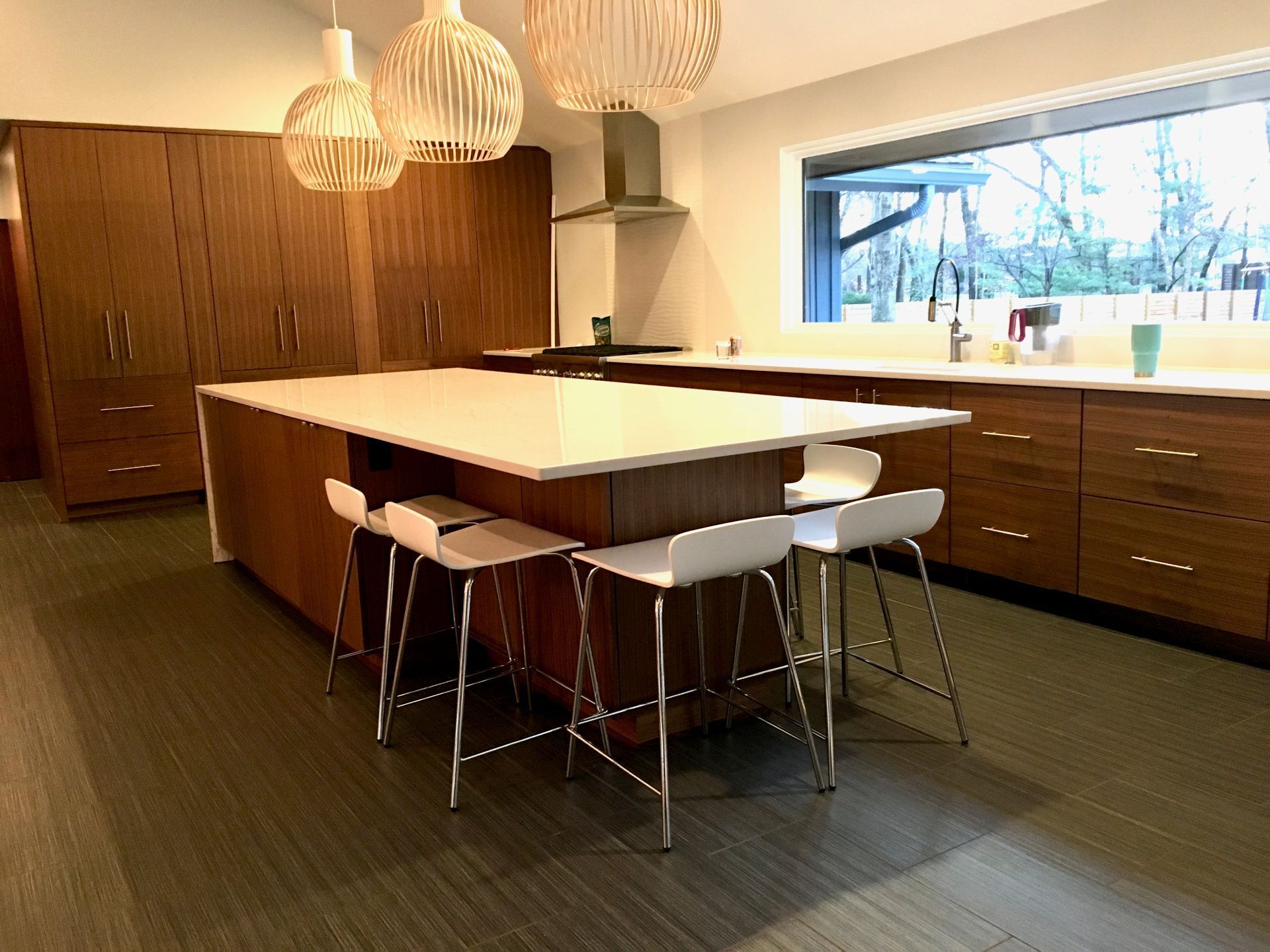 A kitchen with a large island and stools and a large window.