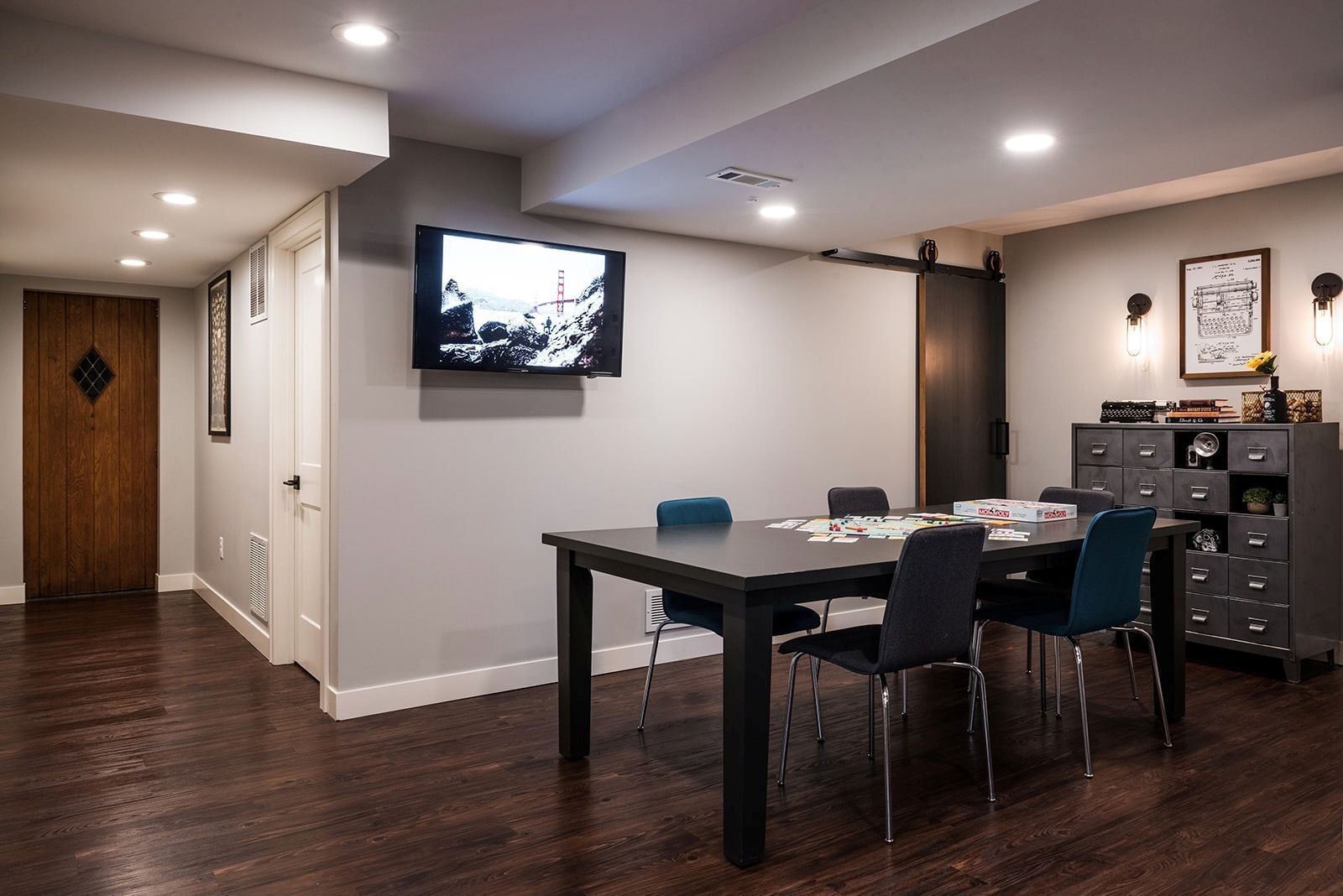 A basement with a table and chairs and a flat screen tv on the wall.