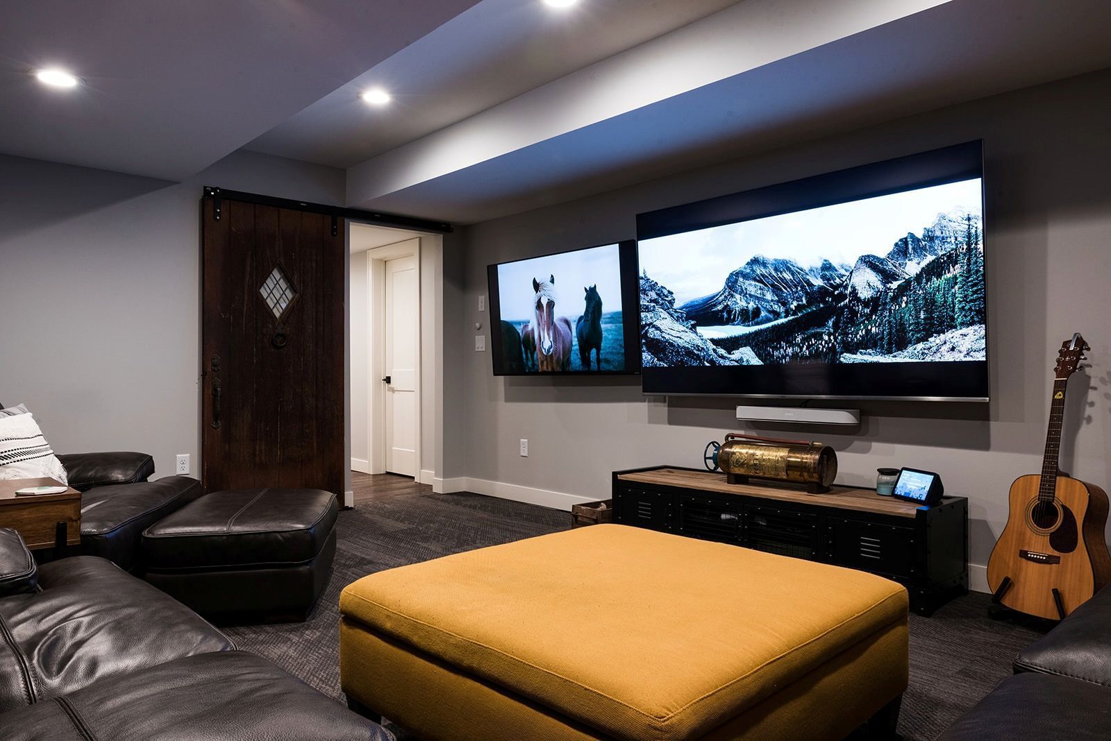 A living room with a couch , ottoman , guitar and two televisions.