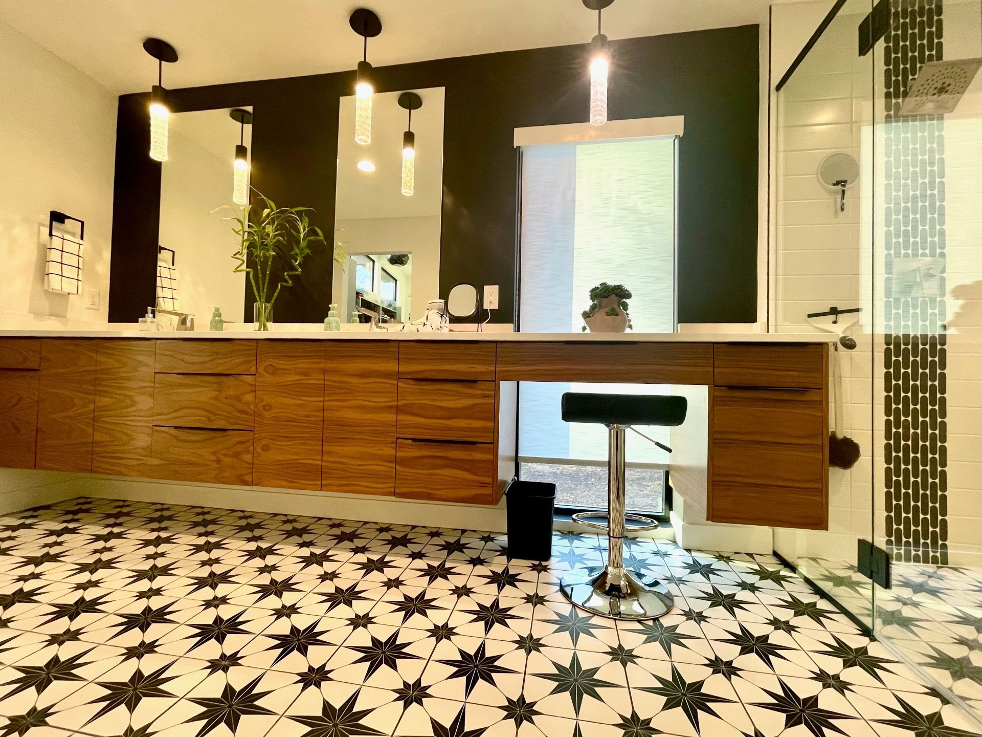 A bathroom with a black and white tile floor , two sinks , two mirrors and a stool.