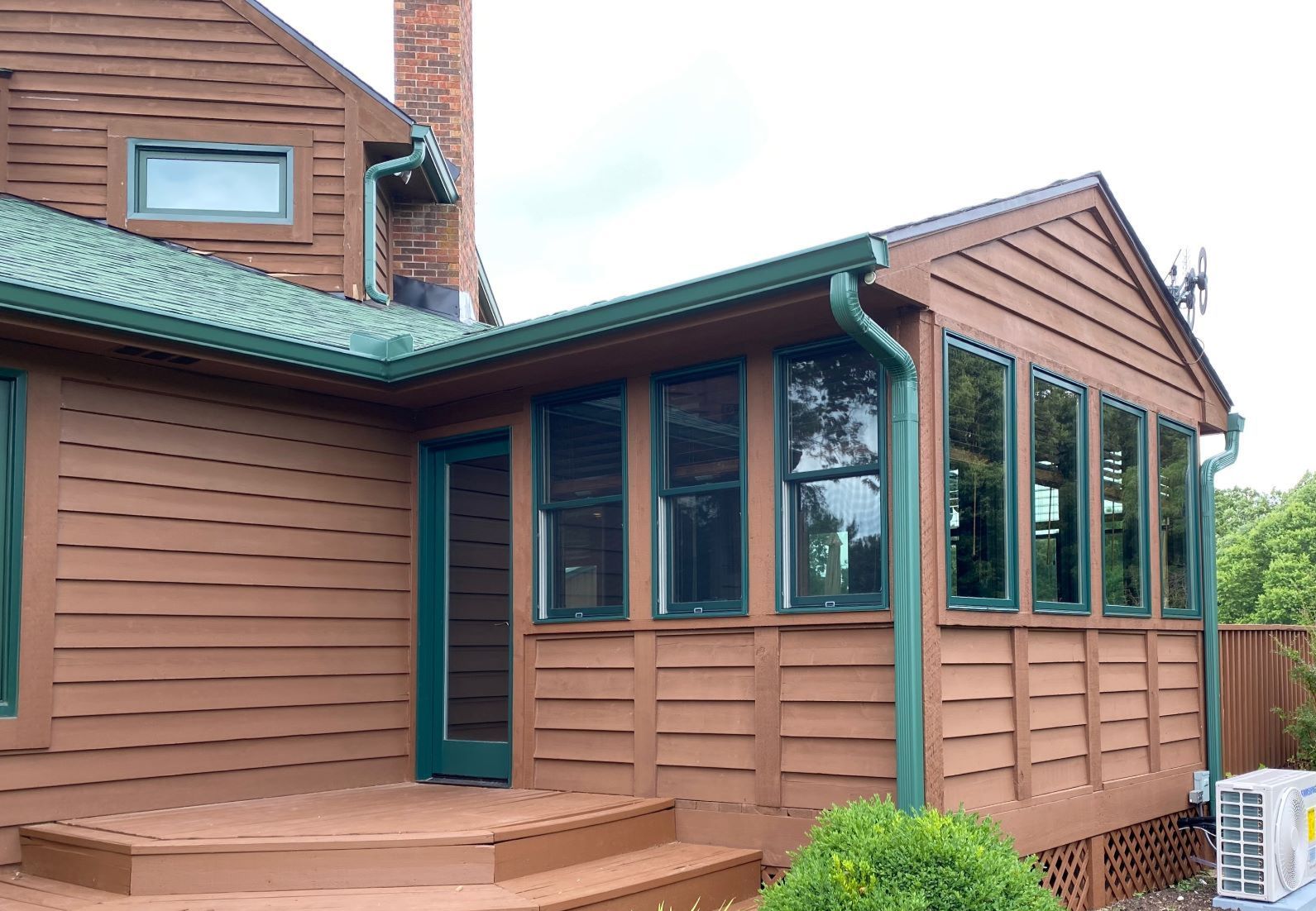 A brown house with a green roof and a sunroom