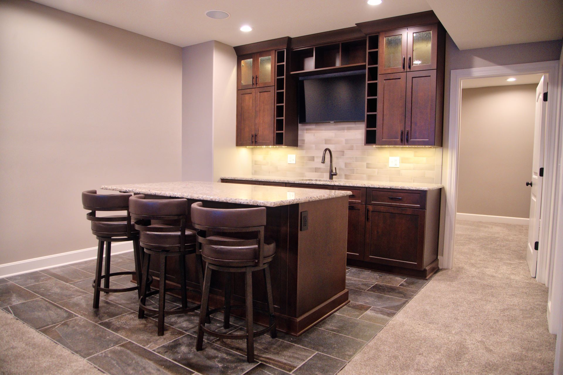 A kitchen with a large island and stools in a basement.