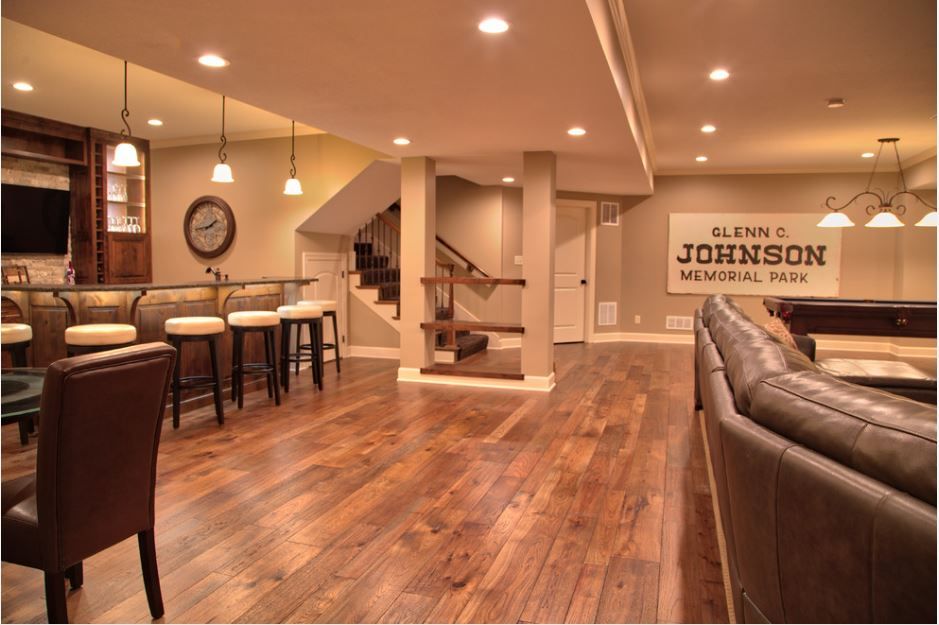 A basement with hardwood floors , a bar , a couch , chairs and a pool table.
