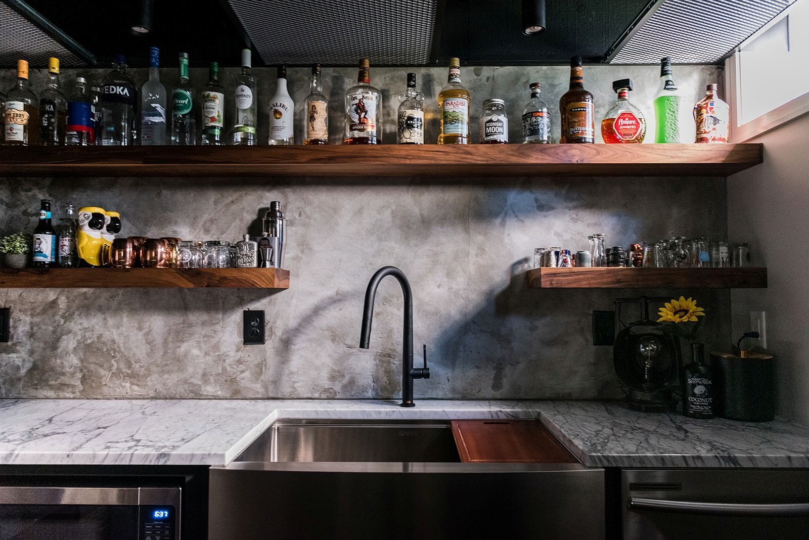 A kitchen with a sink and shelves filled with bottles of alcohol.