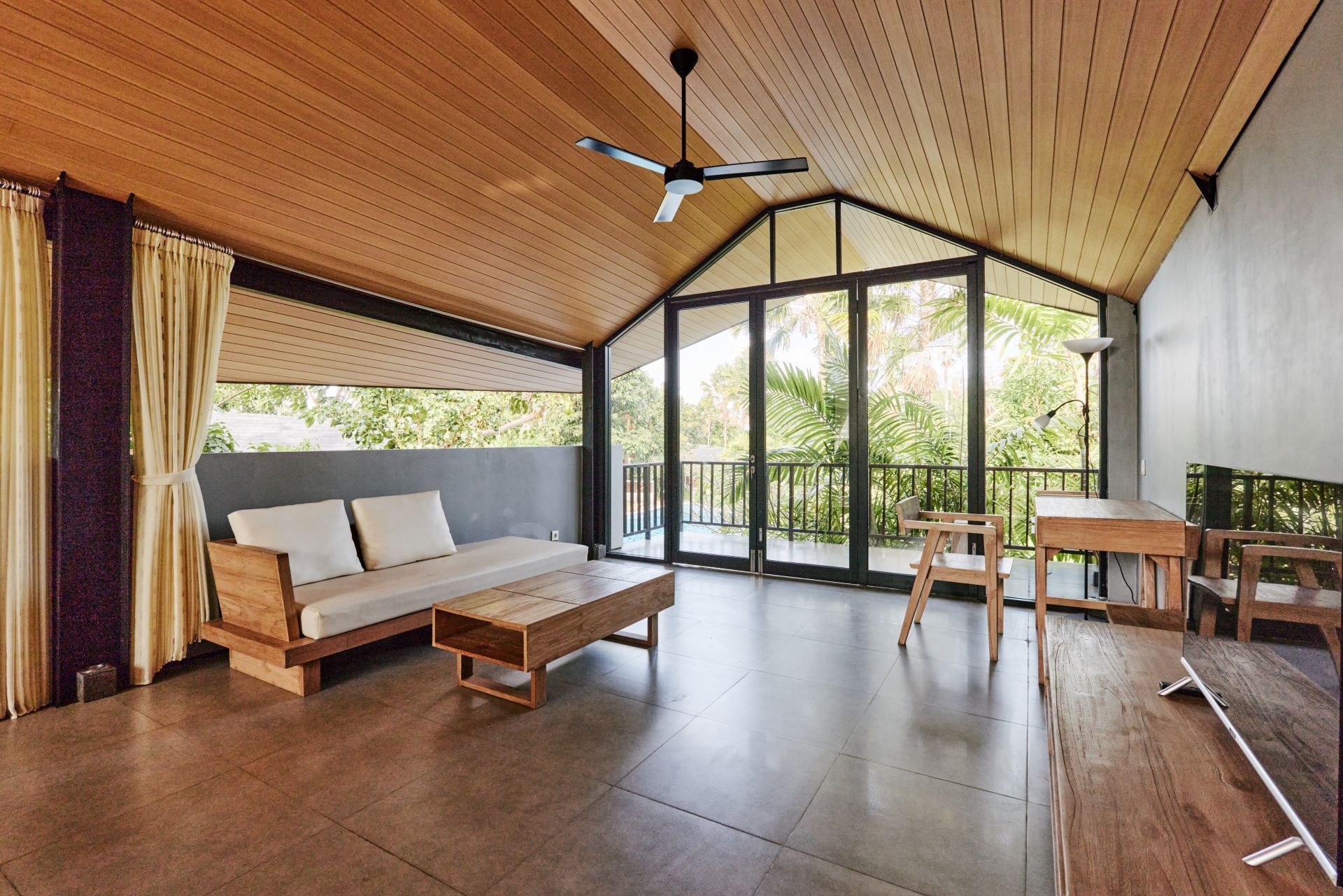 Living room with wooden ceiling and furniture, large glass doors to a balcony, and a neutral color palette.