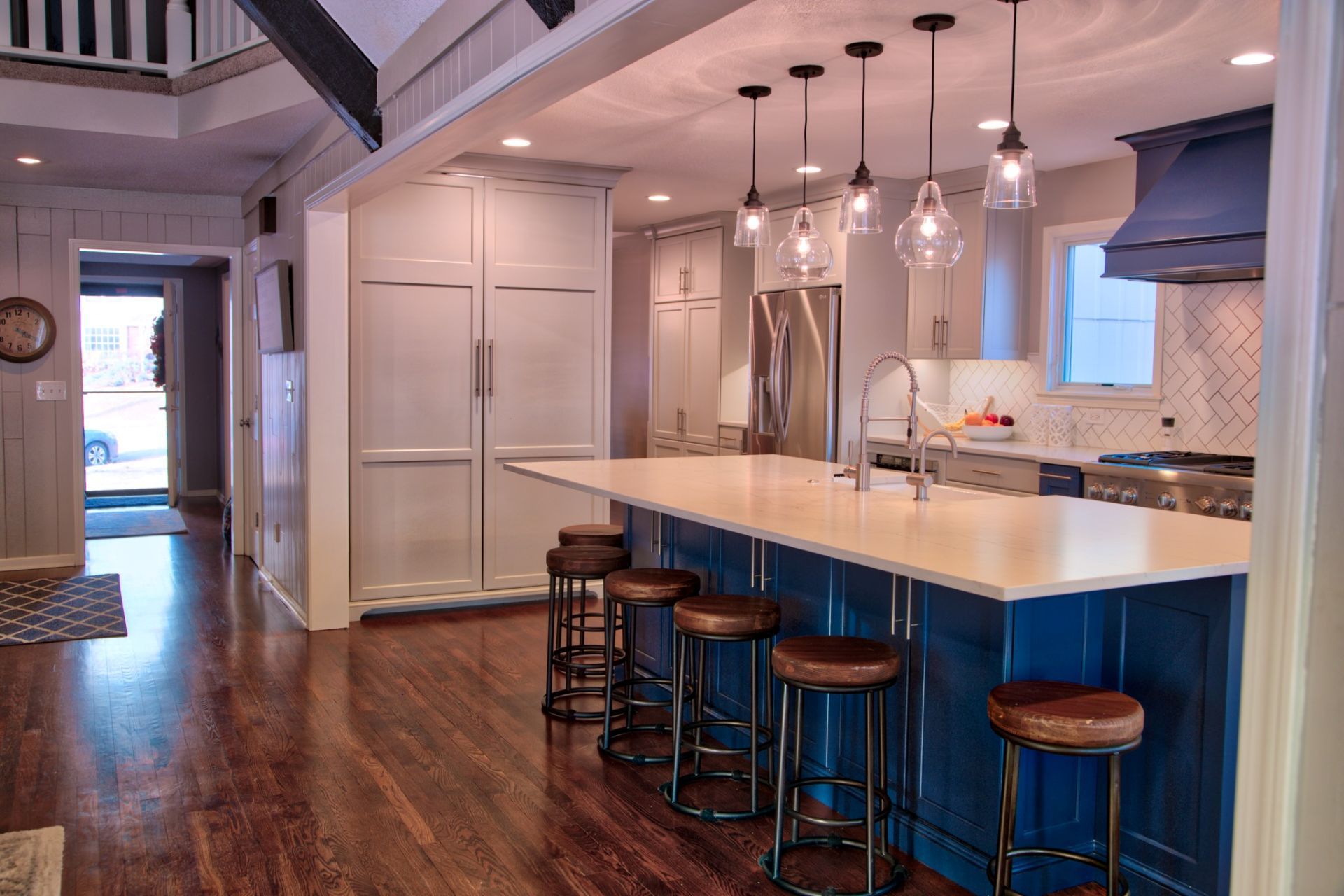 A kitchen with blue cabinets and white counter tops and stools.