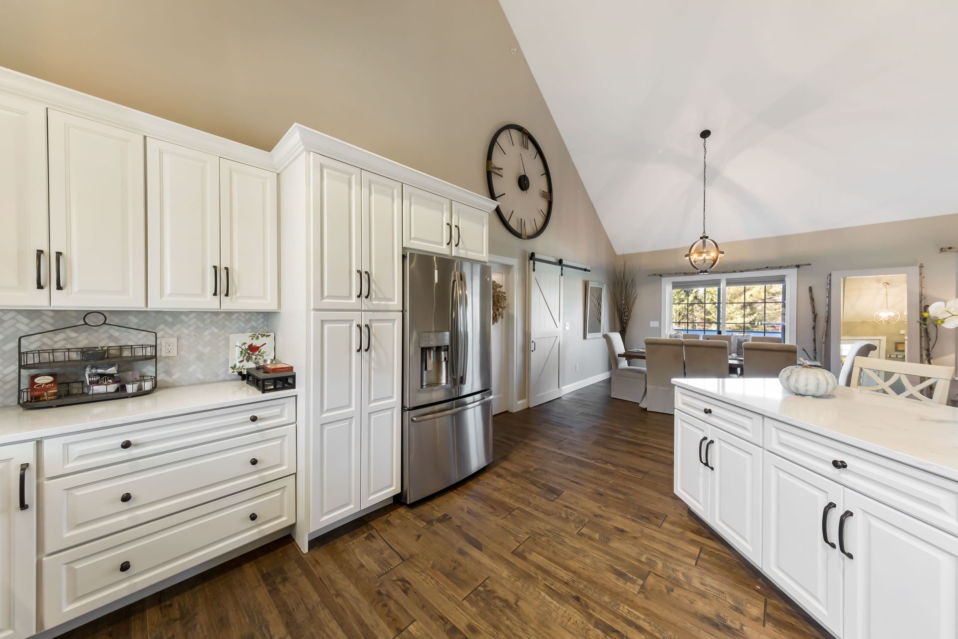 White kitchen with stainless steel appliances, wood floors, and a large clock.