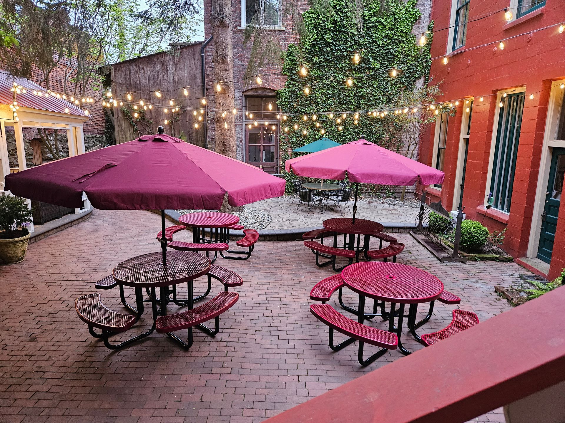 A brick courtyard with red picnic tables and purple umbrellas.