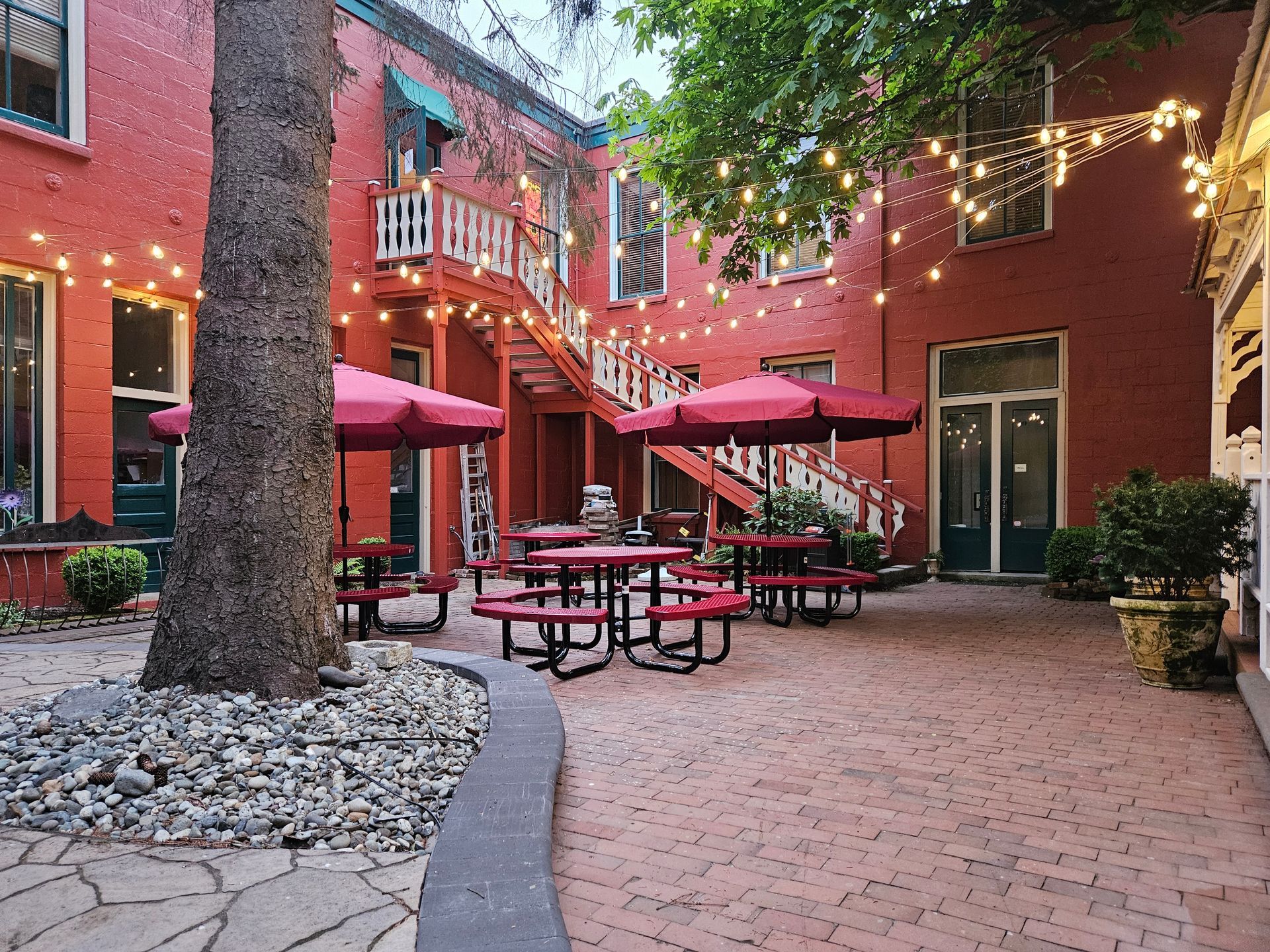 A courtyard with tables and umbrellas in front of a red building.