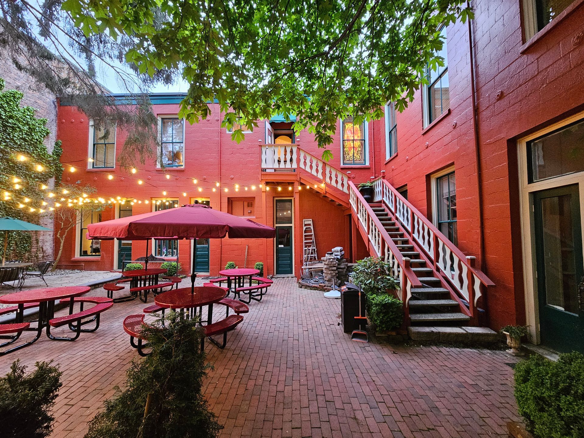 A courtyard with tables and umbrellas in front of a red building.