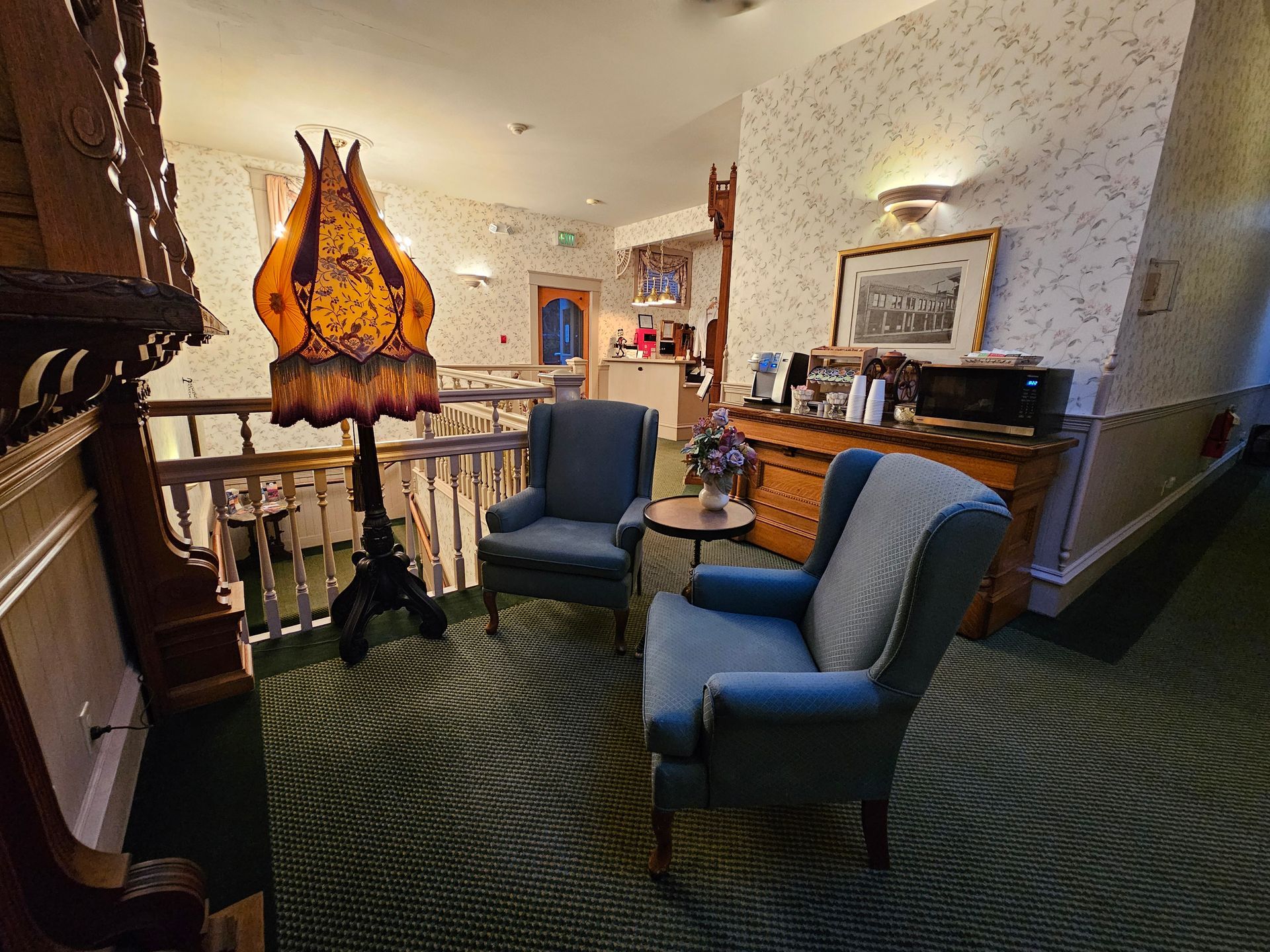 A hallway with chairs , a lamp and a table.