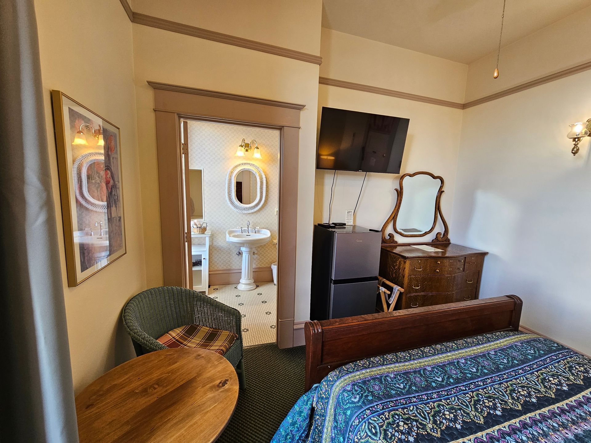 A bedroom with a bed , dresser , chair , mirror and refrigerator.