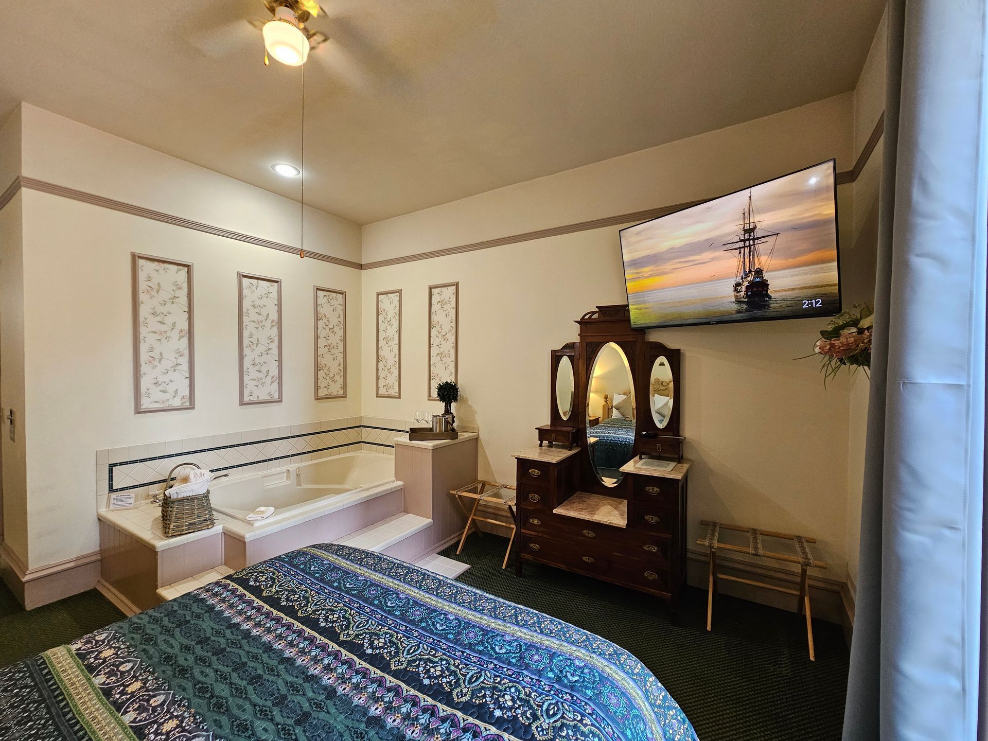 A bedroom with a bed , dresser , television and jacuzzi tub.