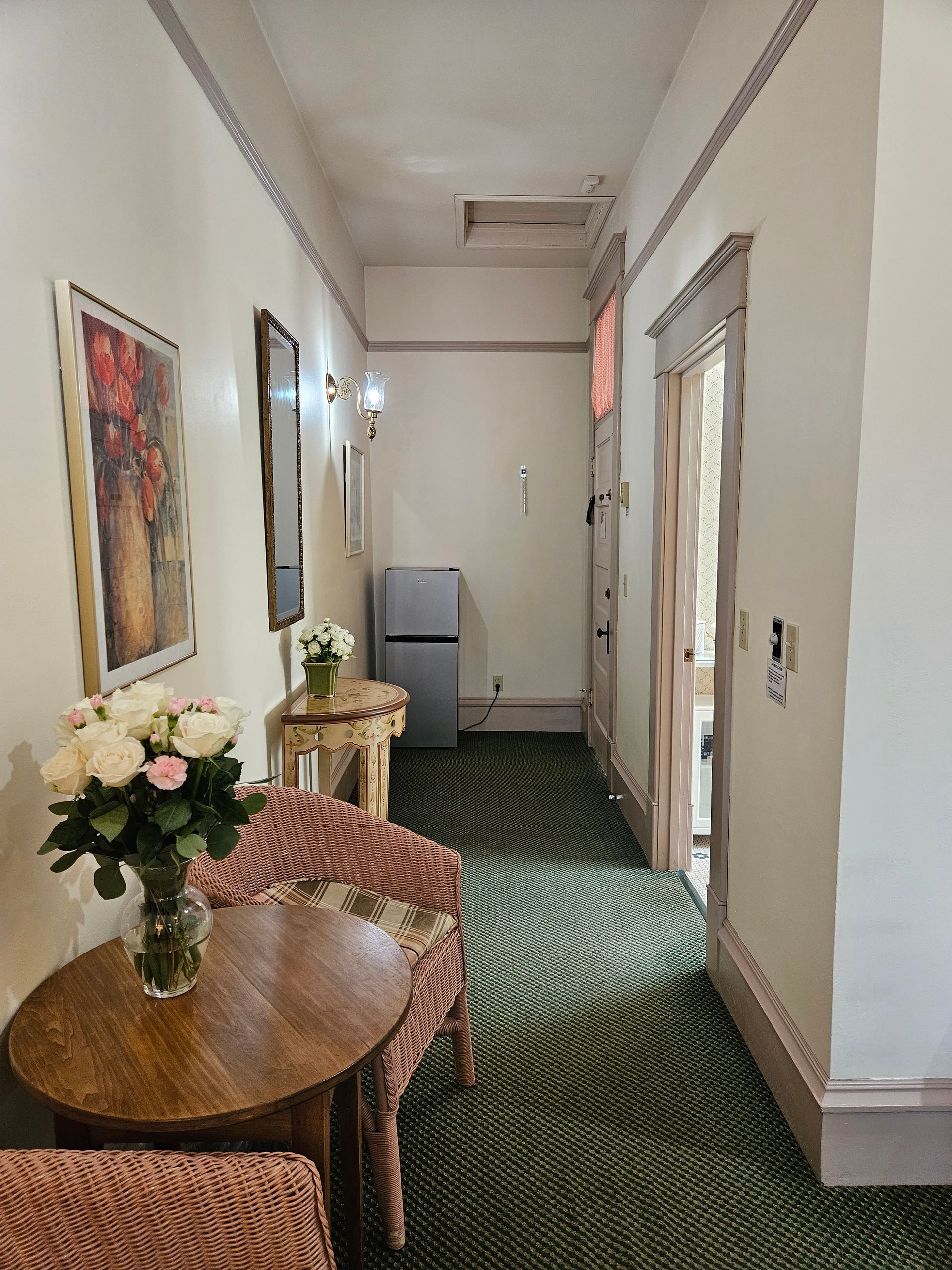 A long hallway with a table and chairs and a vase of flowers.