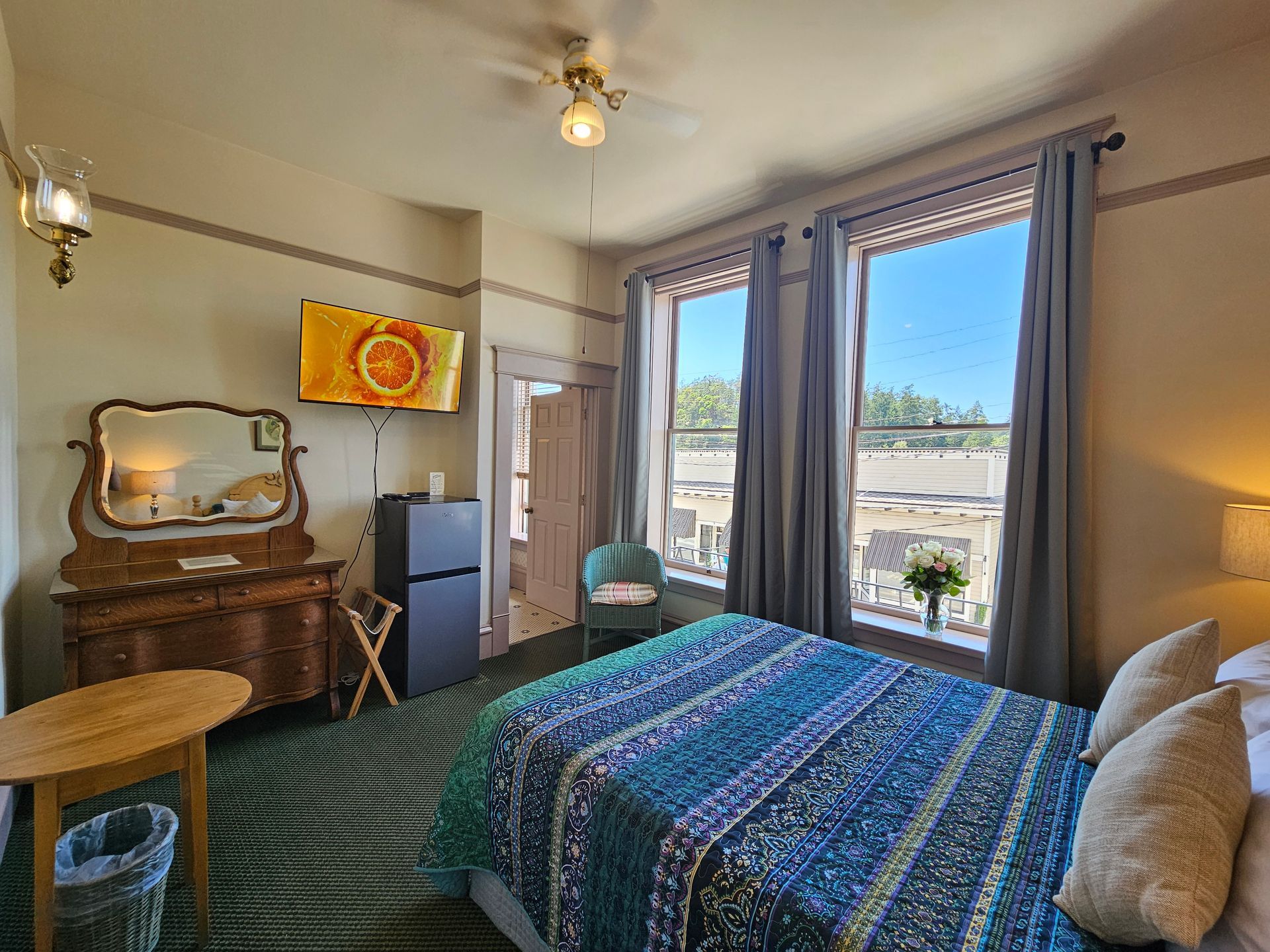 A hotel room with a bed , dresser , refrigerator , mirror and television.