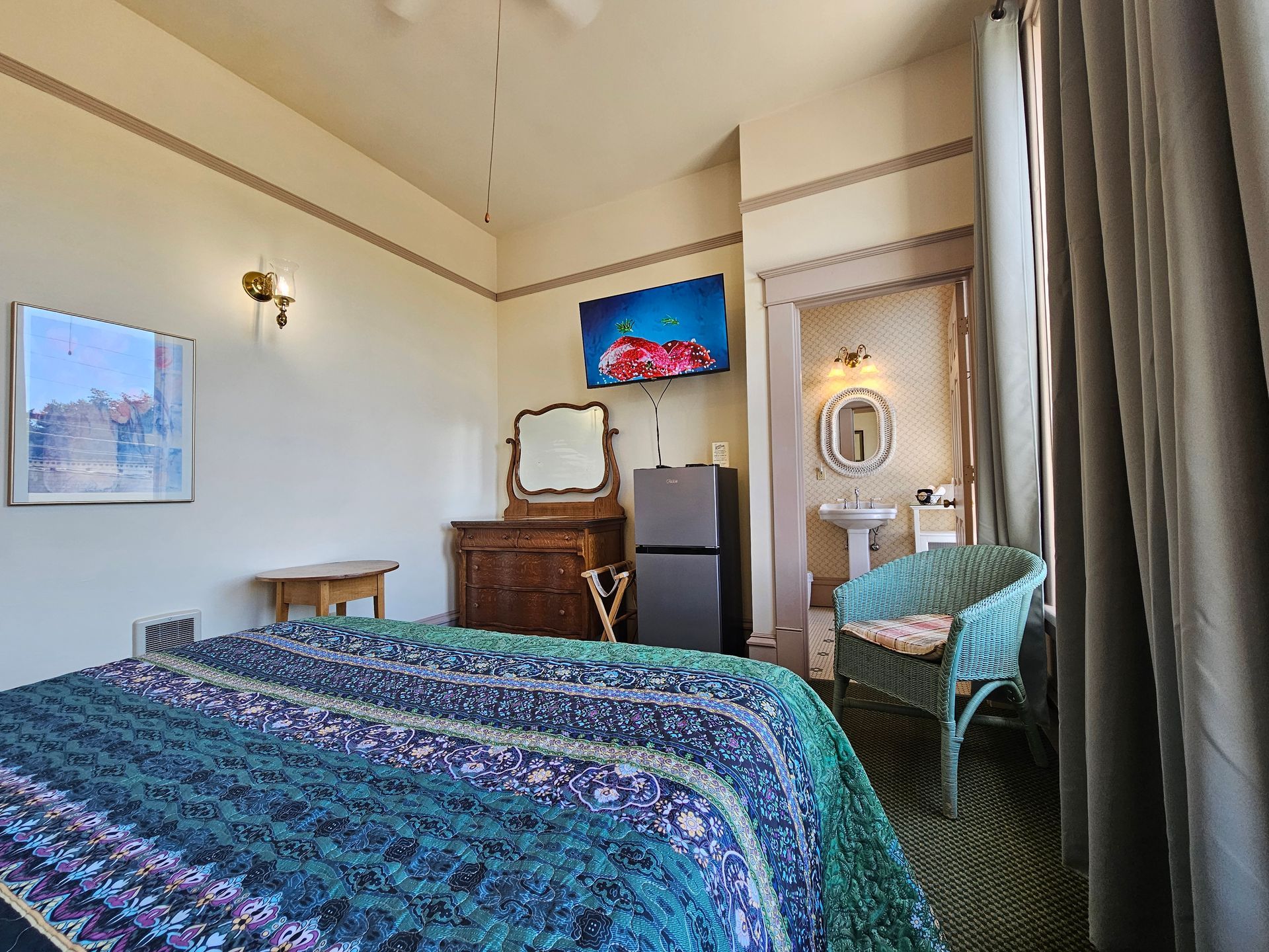 A bedroom with a bed , chair , dresser , refrigerator and sink.